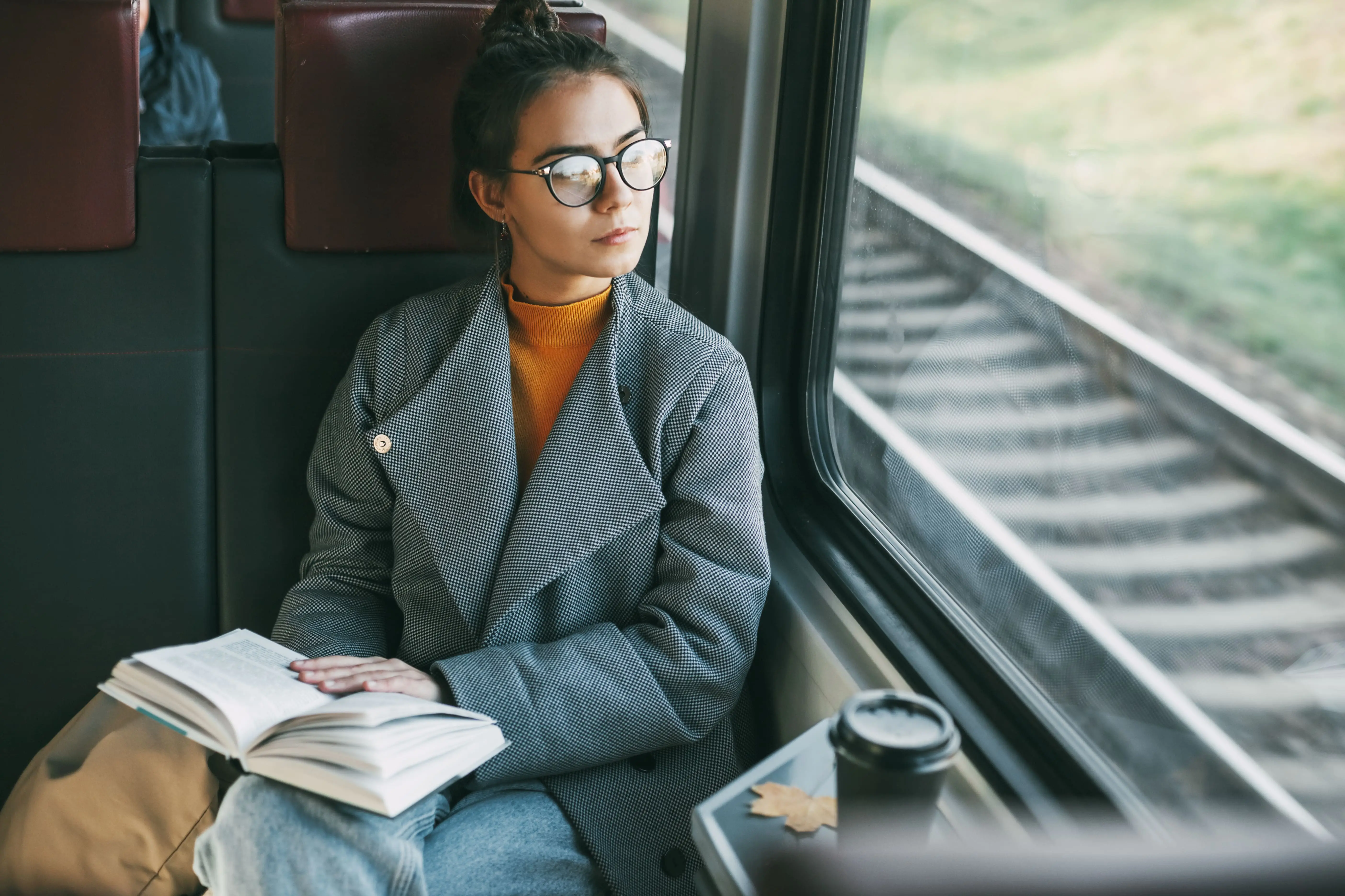Writing Rail Books 1 Train Books: A young woman sits on a train, looking out of the window whilst reading a book.