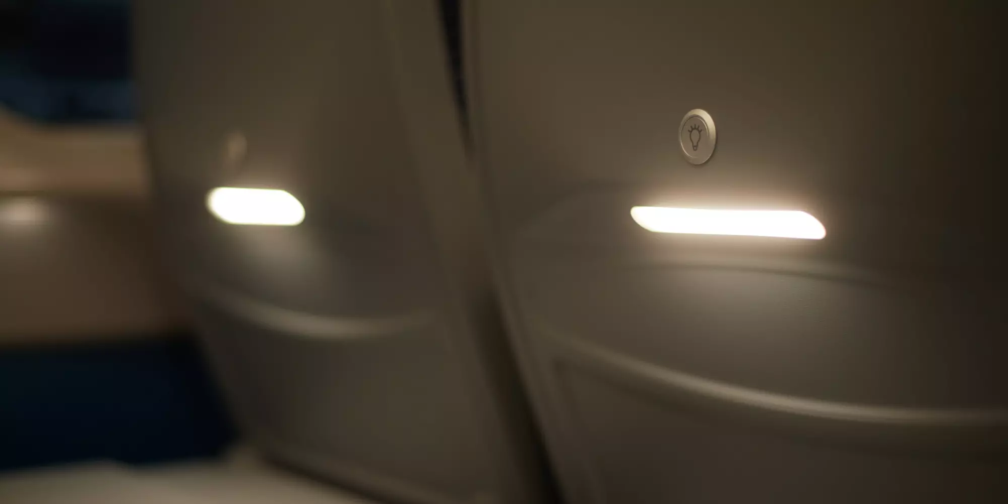 A close up of two seat back lights with on/off buttons. The lights are rectangular. It’s evening so the lights shine clearly.