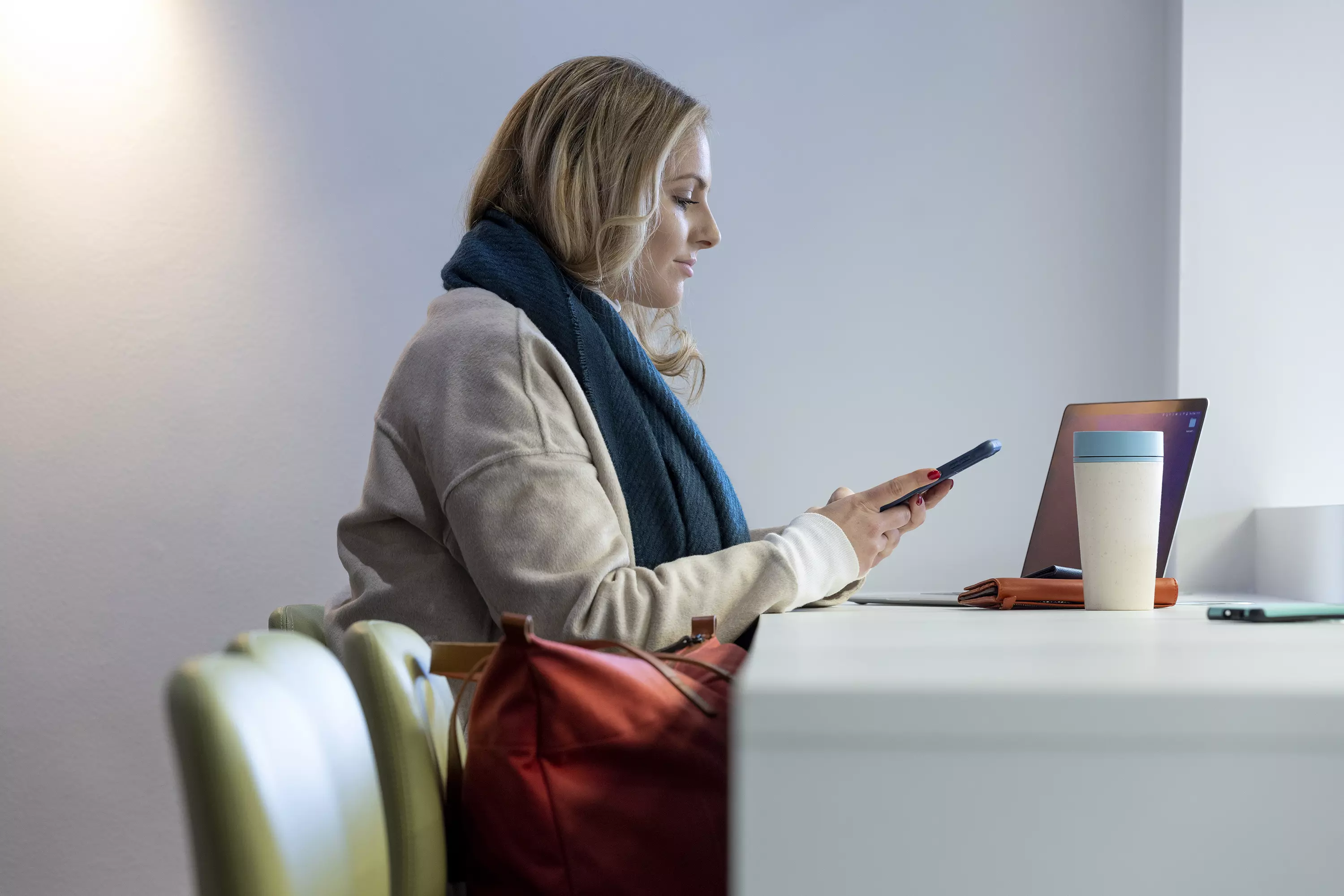 A women sitting and working on her phone with her laptop in front of her