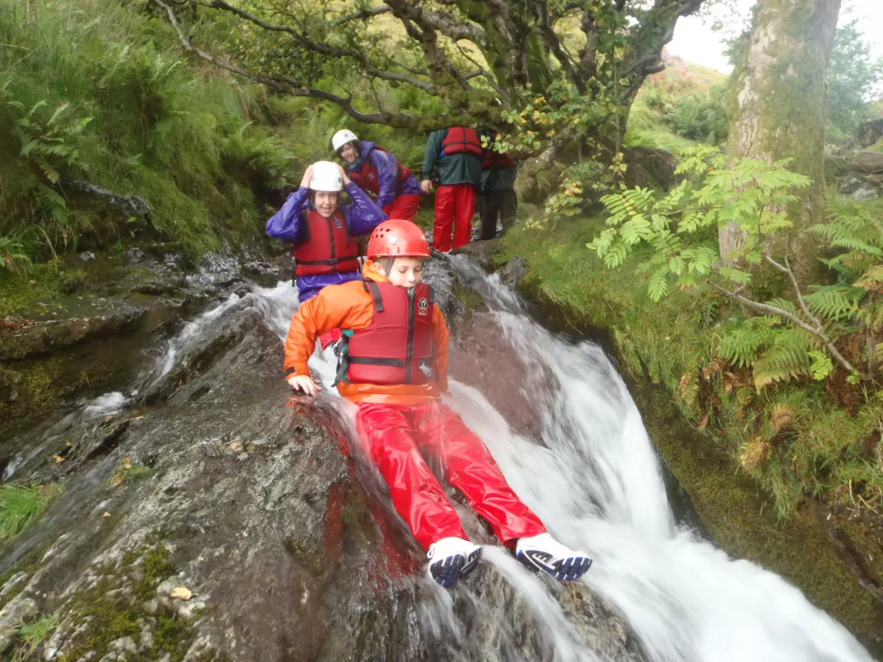 Water adventure with girl in a wetsuit sliding down the waterfall