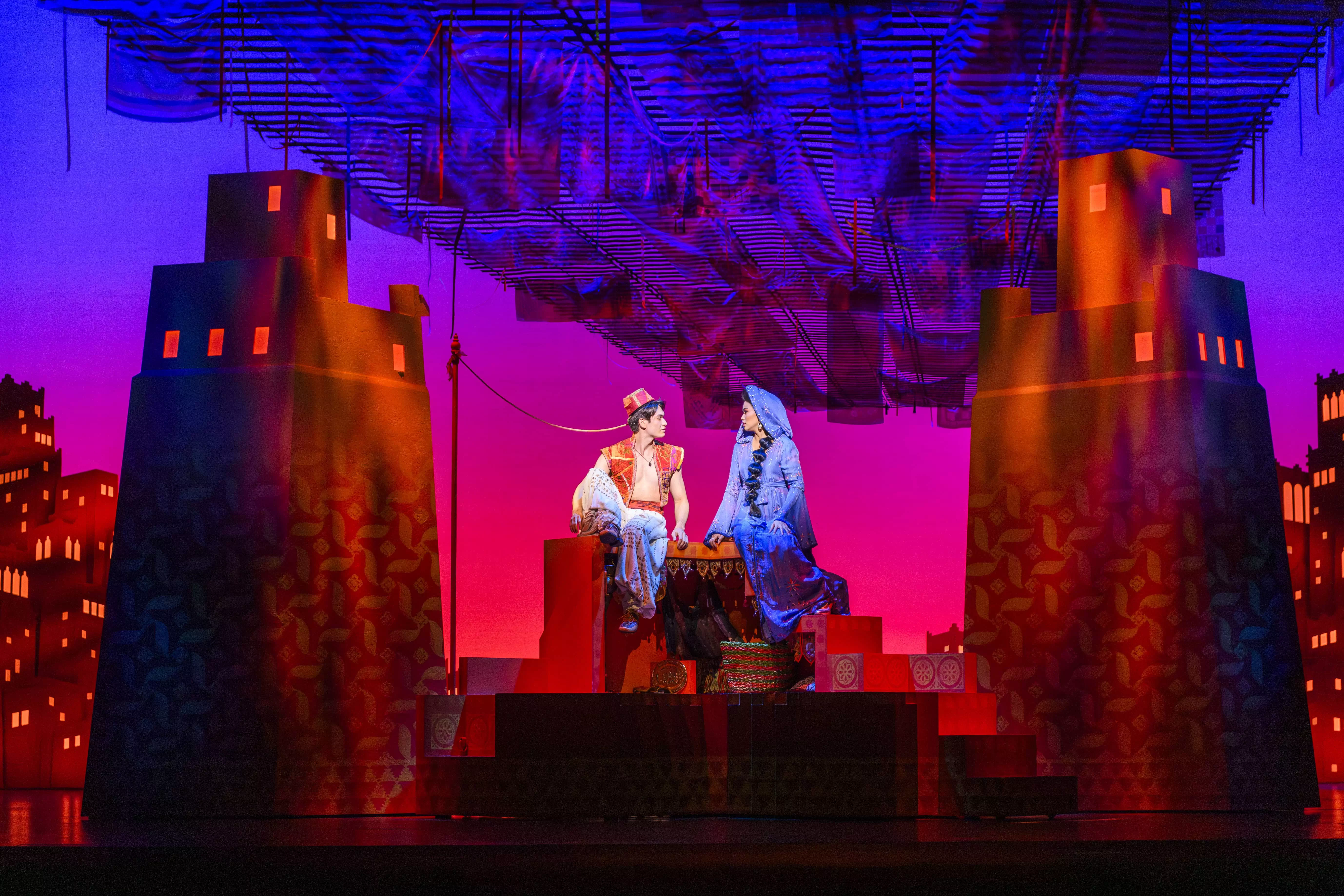 Aladdin and Jasmine on the magic carpet with silhouettes of the city buildings