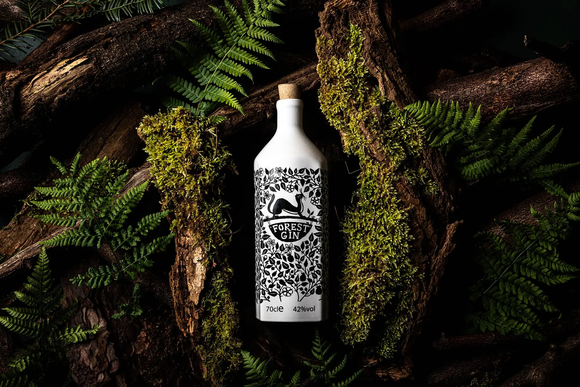 A white bottle of Forest Gin in a woodland setting, surrounded by green leaves and branches.