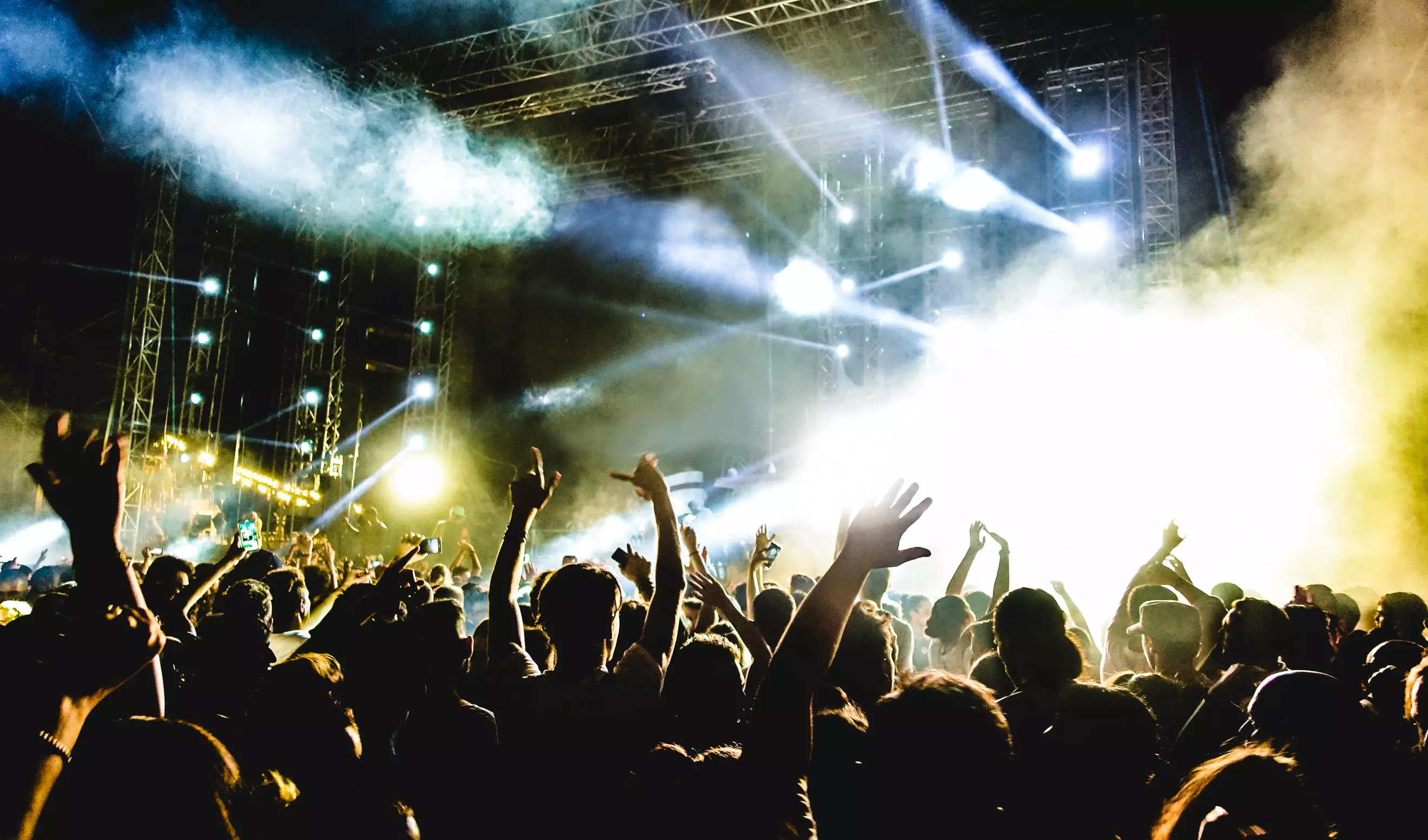 A crowd of people dance and raise their hands in the lights at a club night.