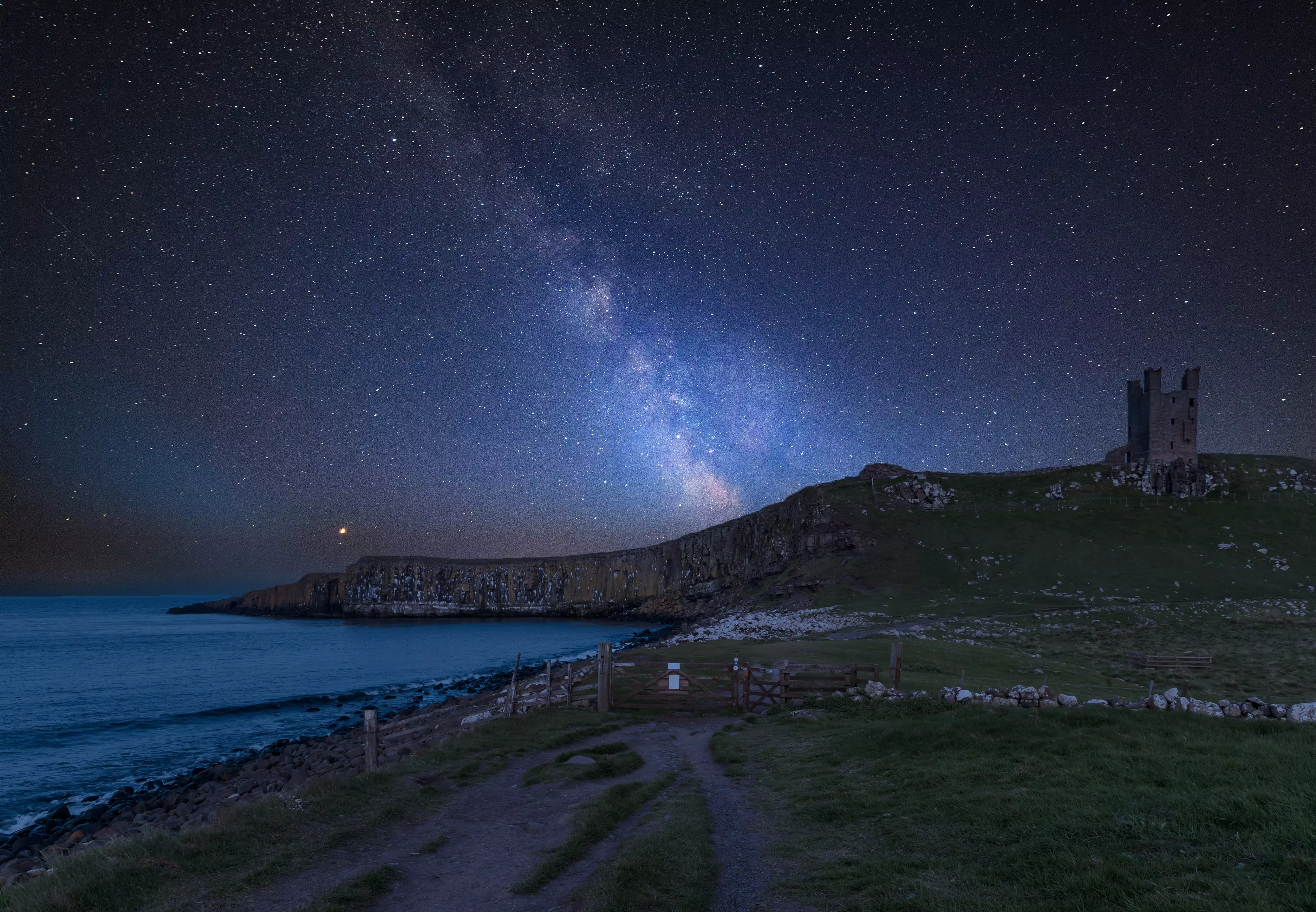 Stunning Milky Way composite image over landscape of Dunstanburgh Castle on Northumberland coastline