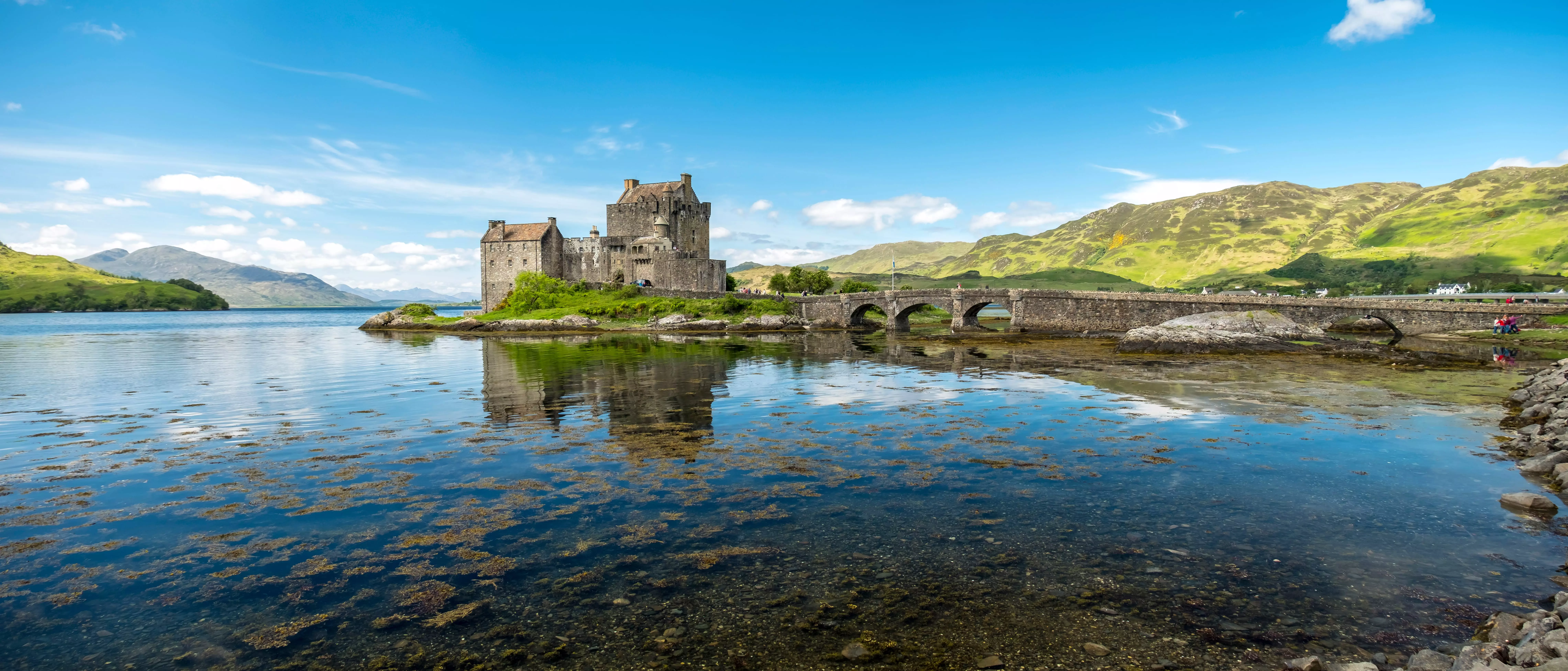 Ruins of Eilean Castle with a loch to the left and countryside hills in the background.