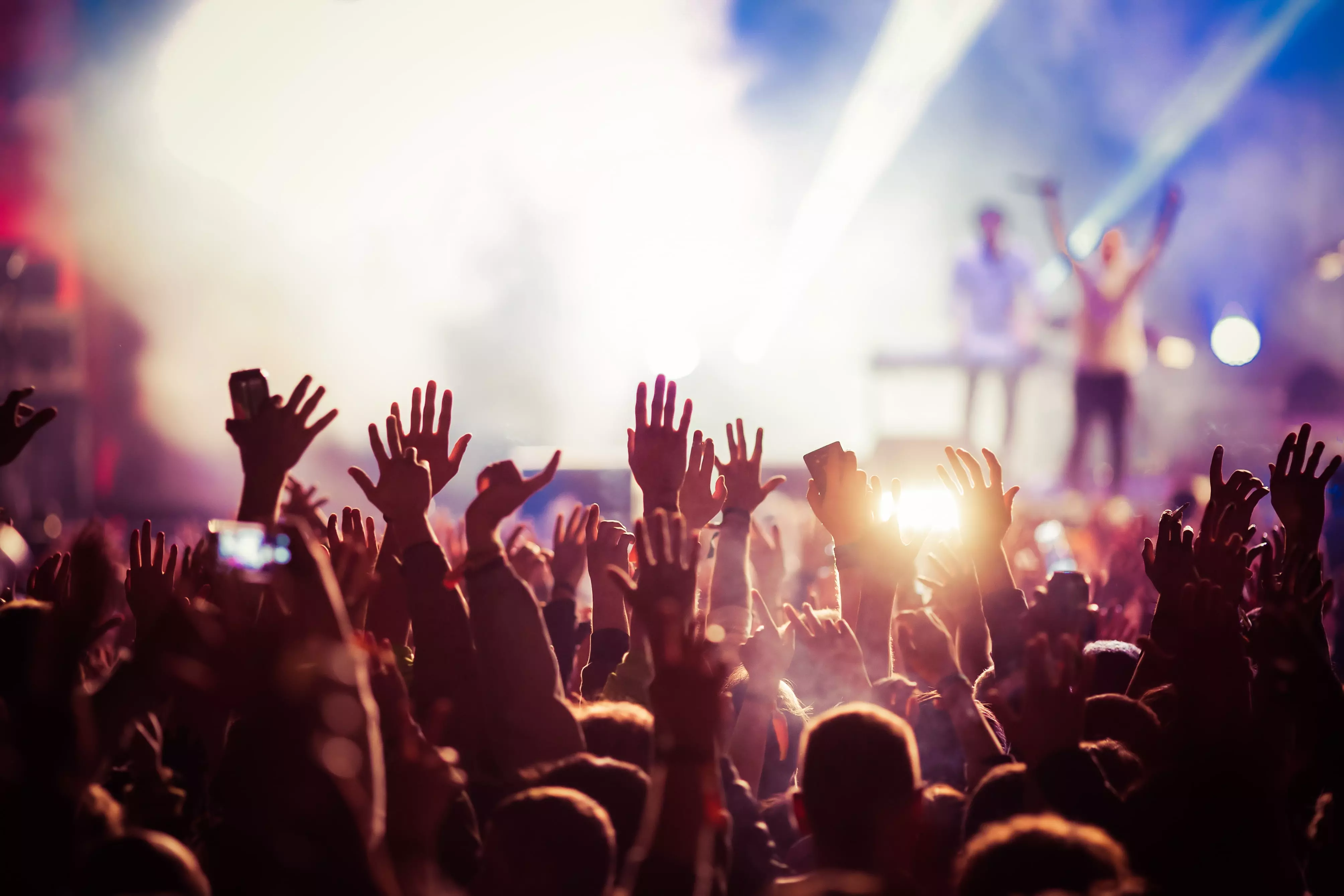 A large crowd at a concert raising their hands.