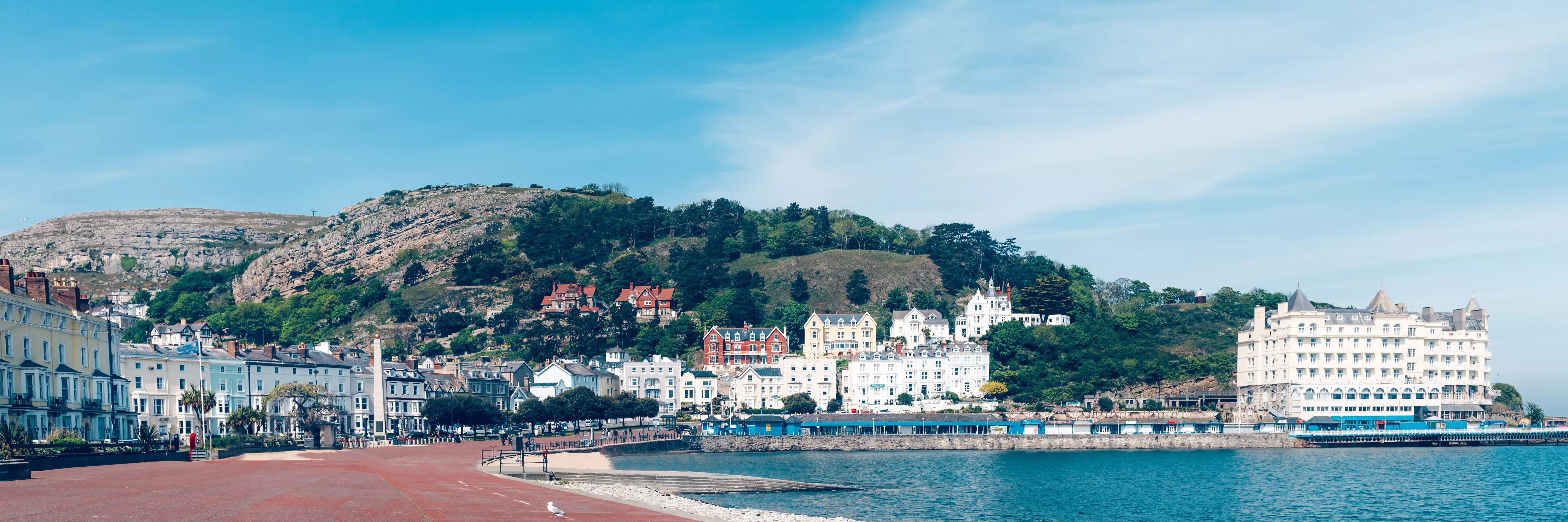 Wide angle photo of Llandudno showing the promenade and a white buildings around the edge bathed in sunlight.