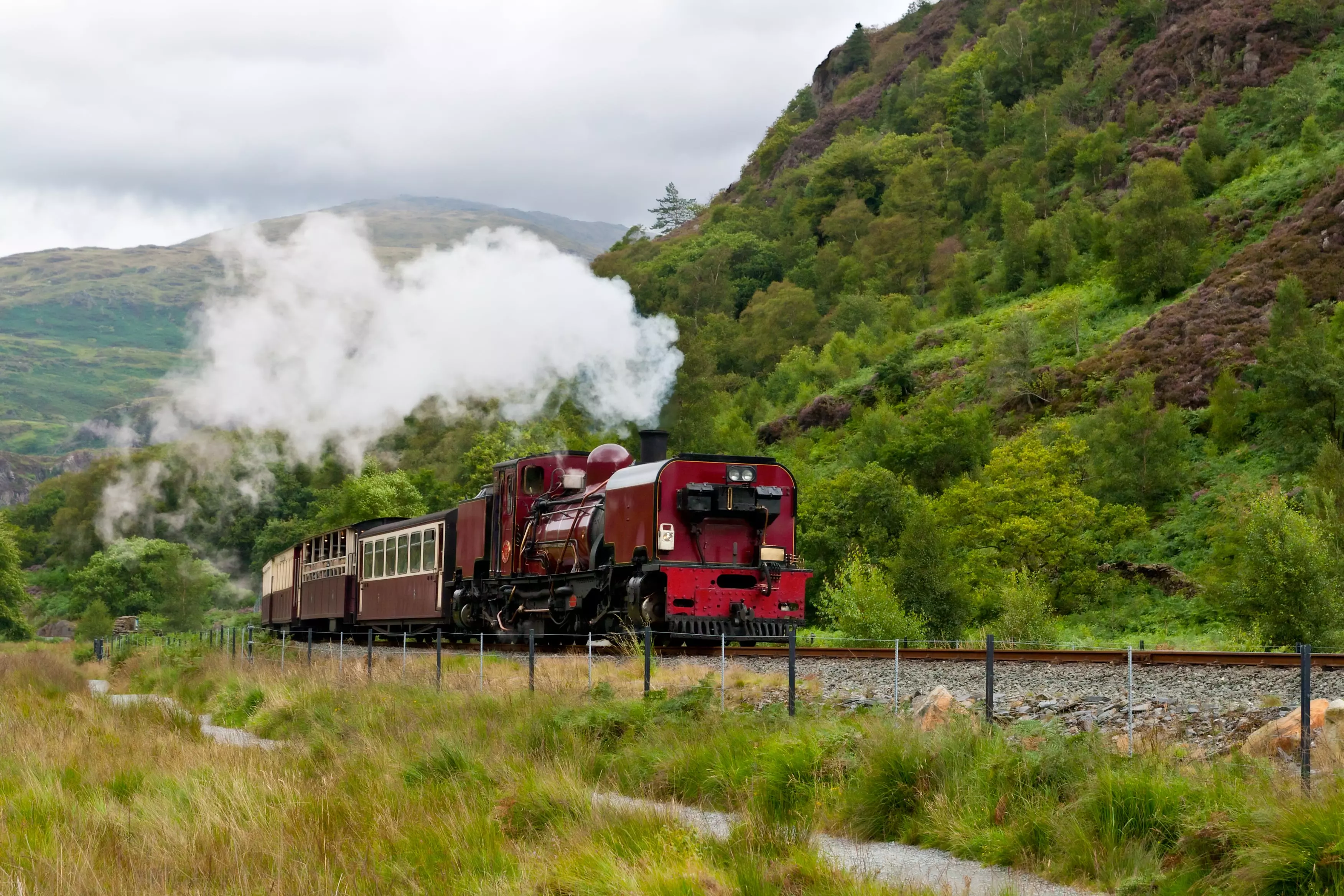 A red steam train pictured in the day going past Snowdonia in Wales.