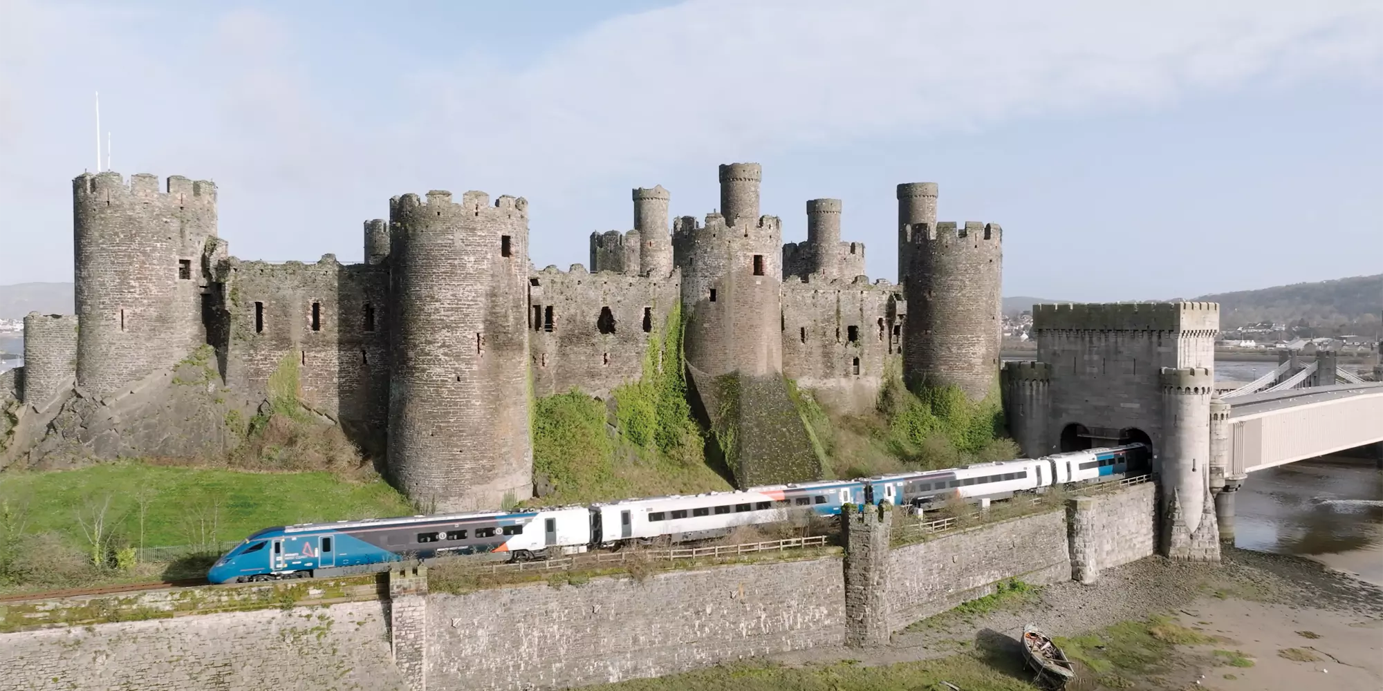 Conwy castle against a blue sky, the new Evero train speeds alongside it.