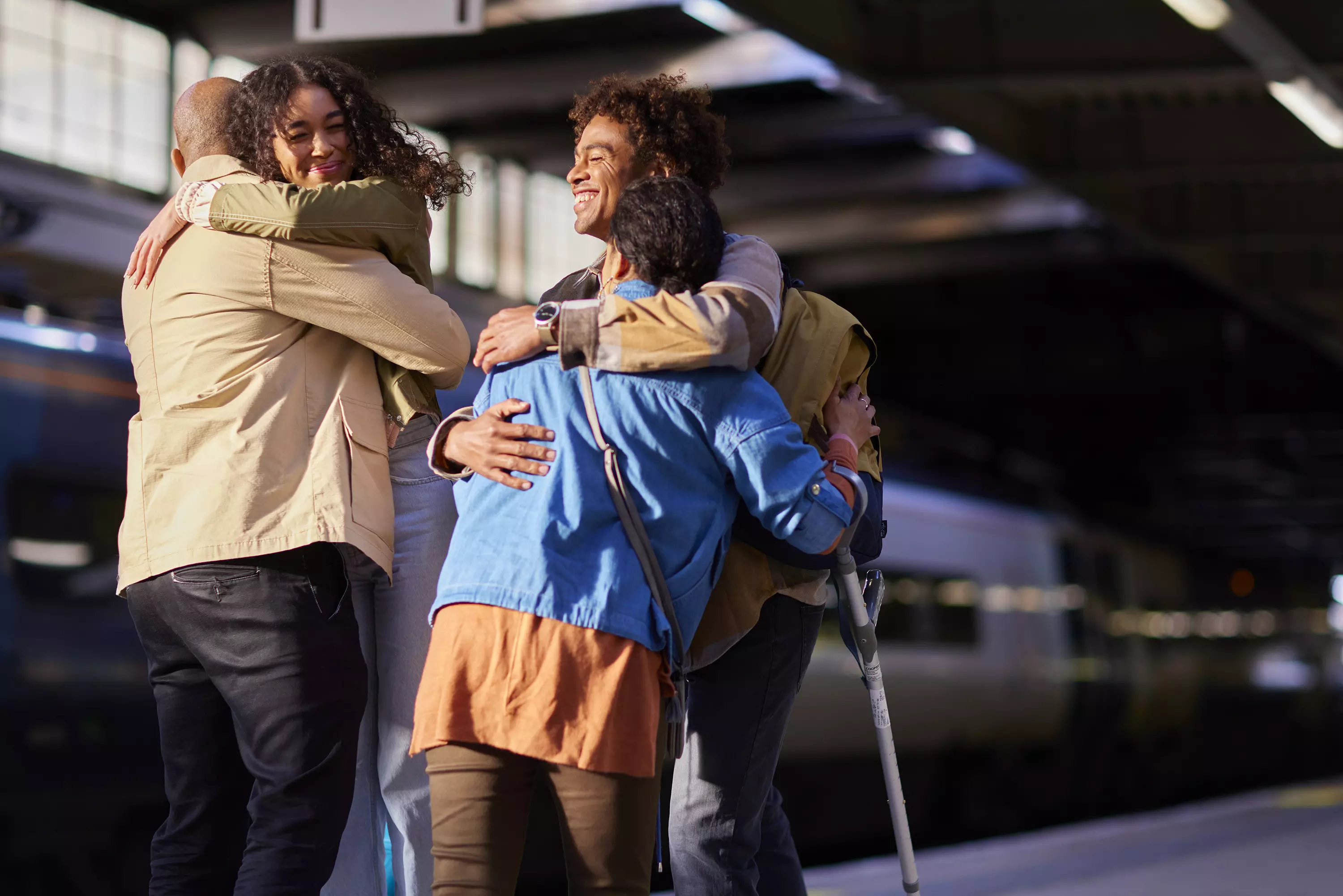 A group of people hugging in a railway station with a train in the background