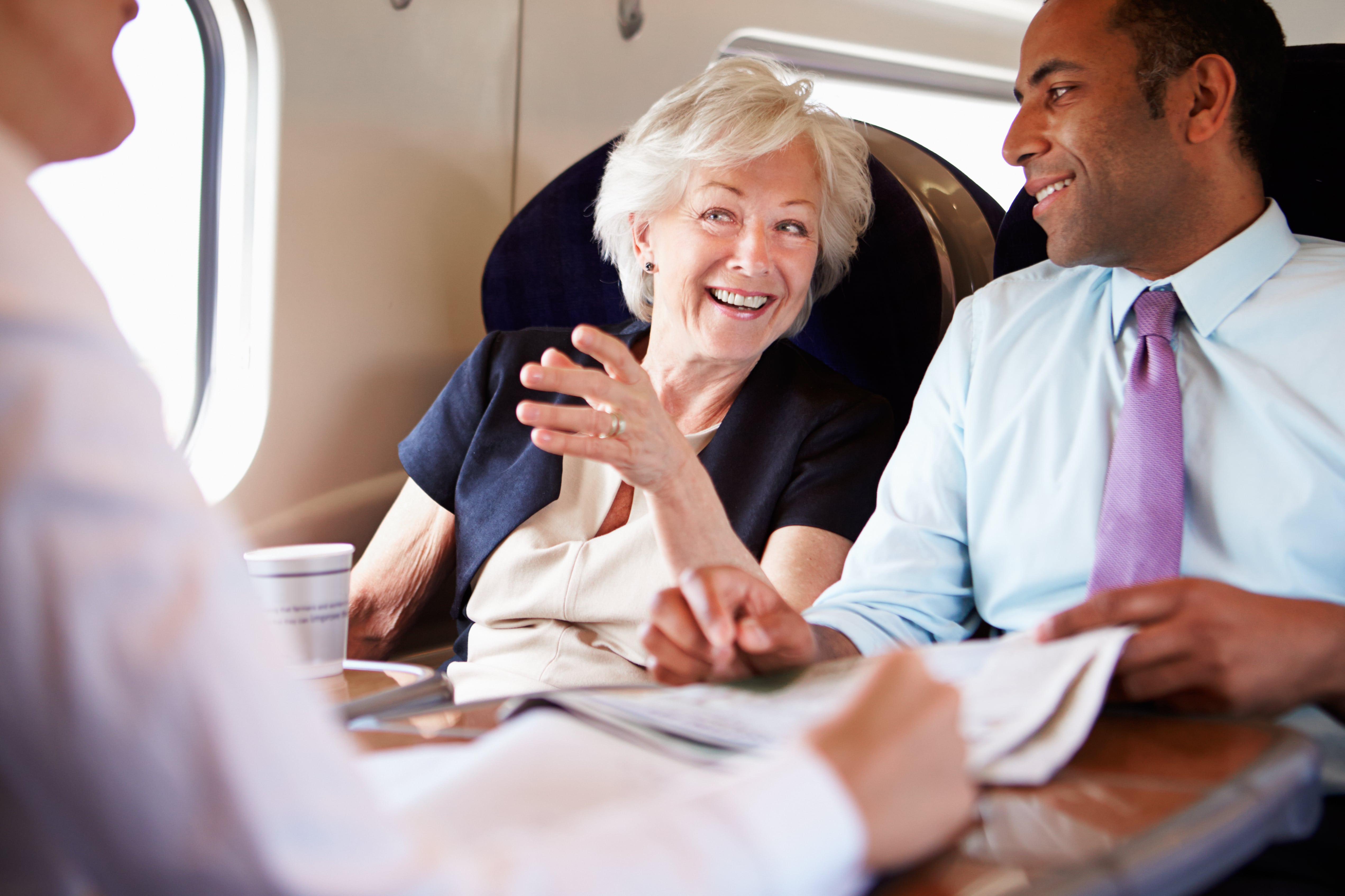 Train Carriages: Business passengers engaged in a lively conversation inside a train, seated around a table with documents and coffee cups