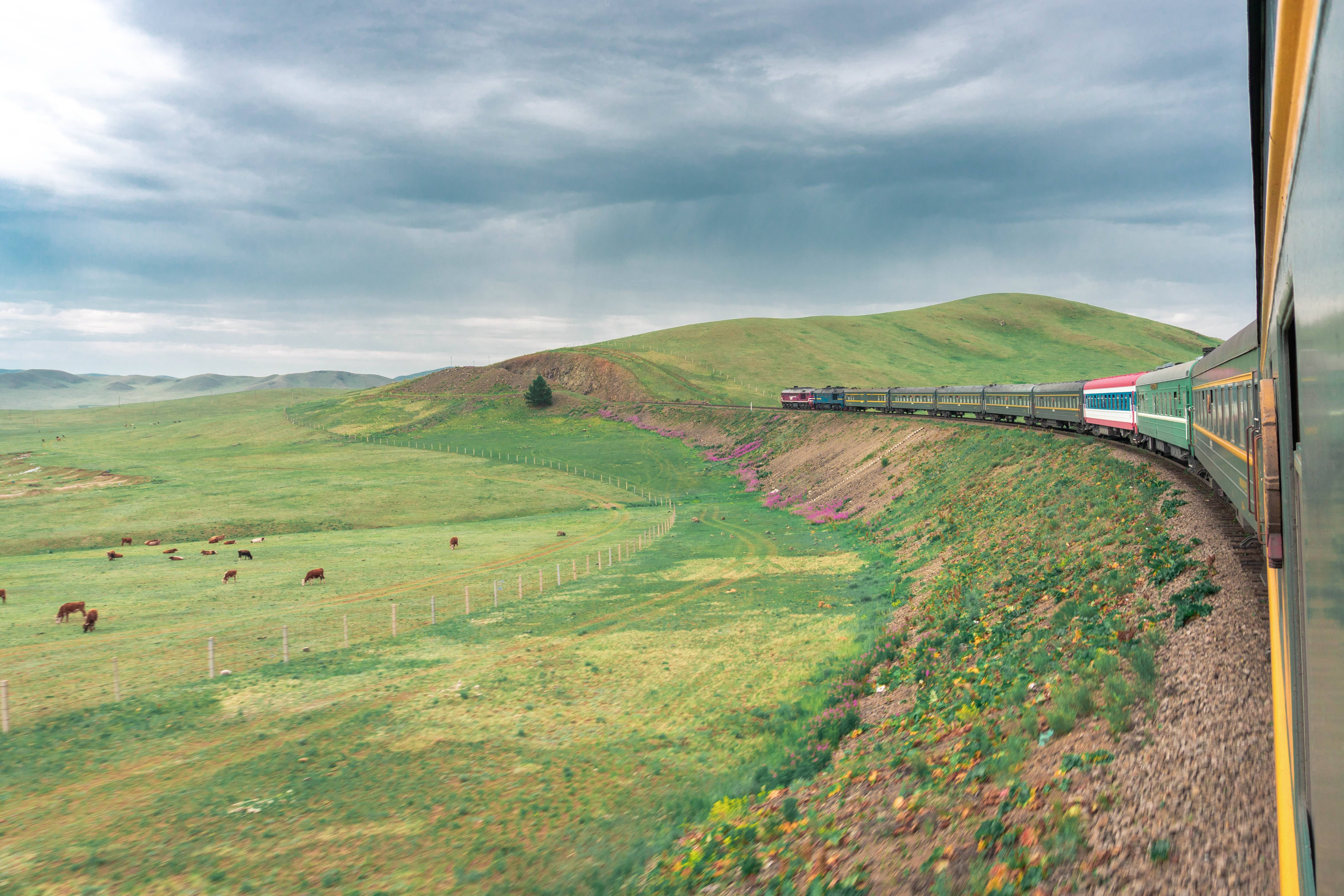 Railway Pioneers: A photo from the window of a train, looking out to see it curving around a bend, with a lush, green field to the left.