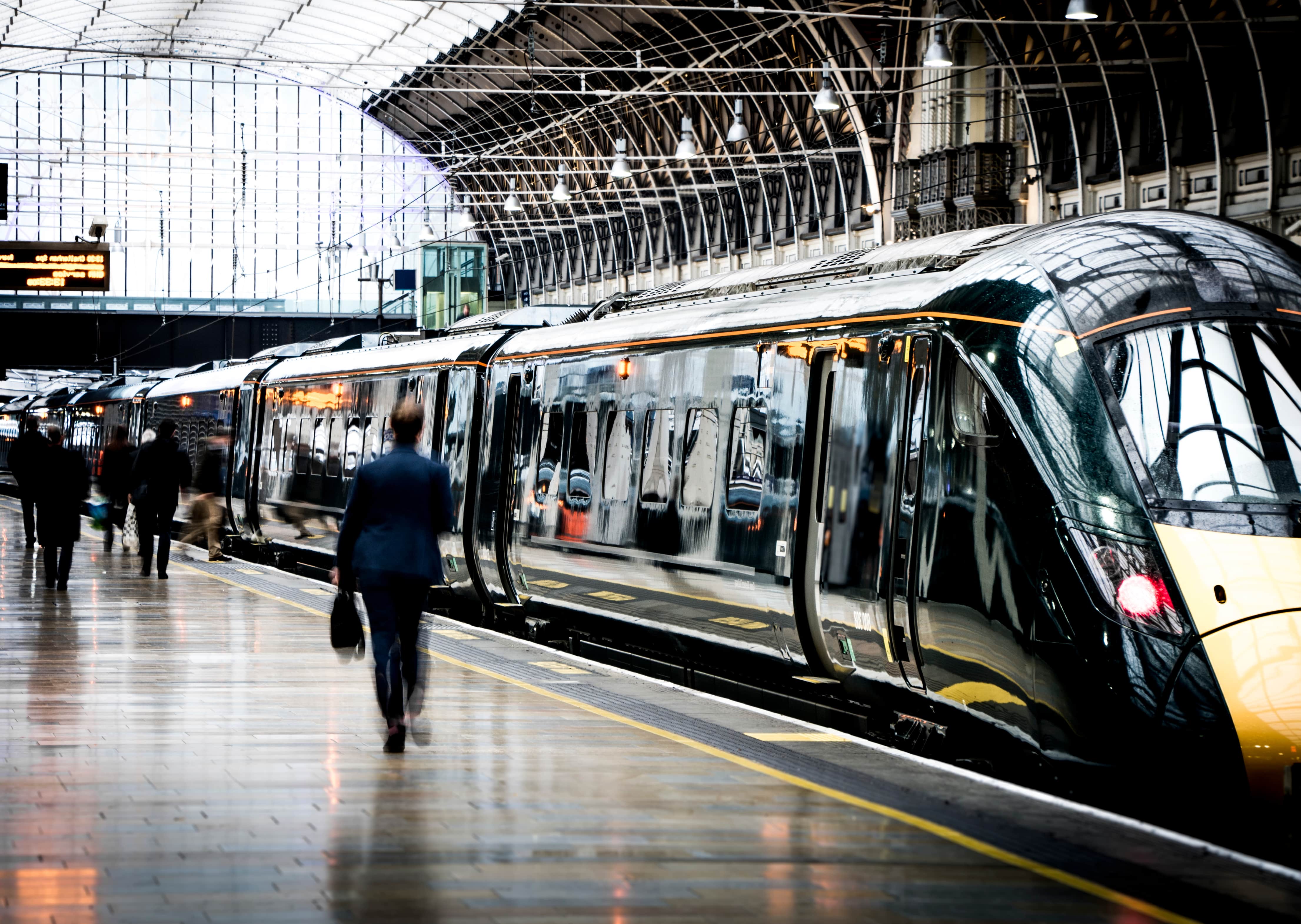 Rail Advertising: A sleek modern train with a dark green and yellow design stationed at a busy railway platform with commuters walking alongside