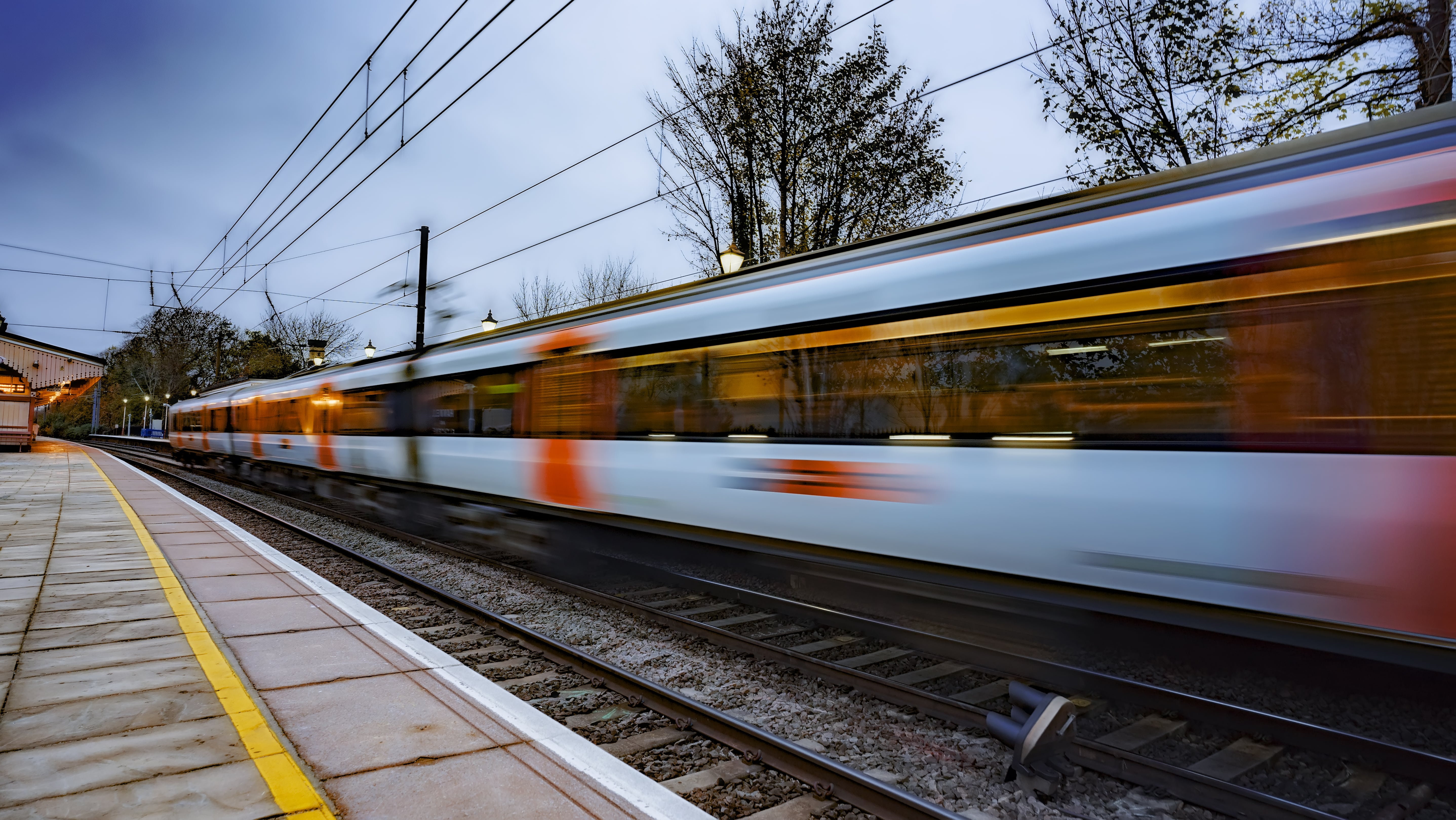 Avanti West Coast: A train speeds through an empty station as grey clouds hang in the sky.