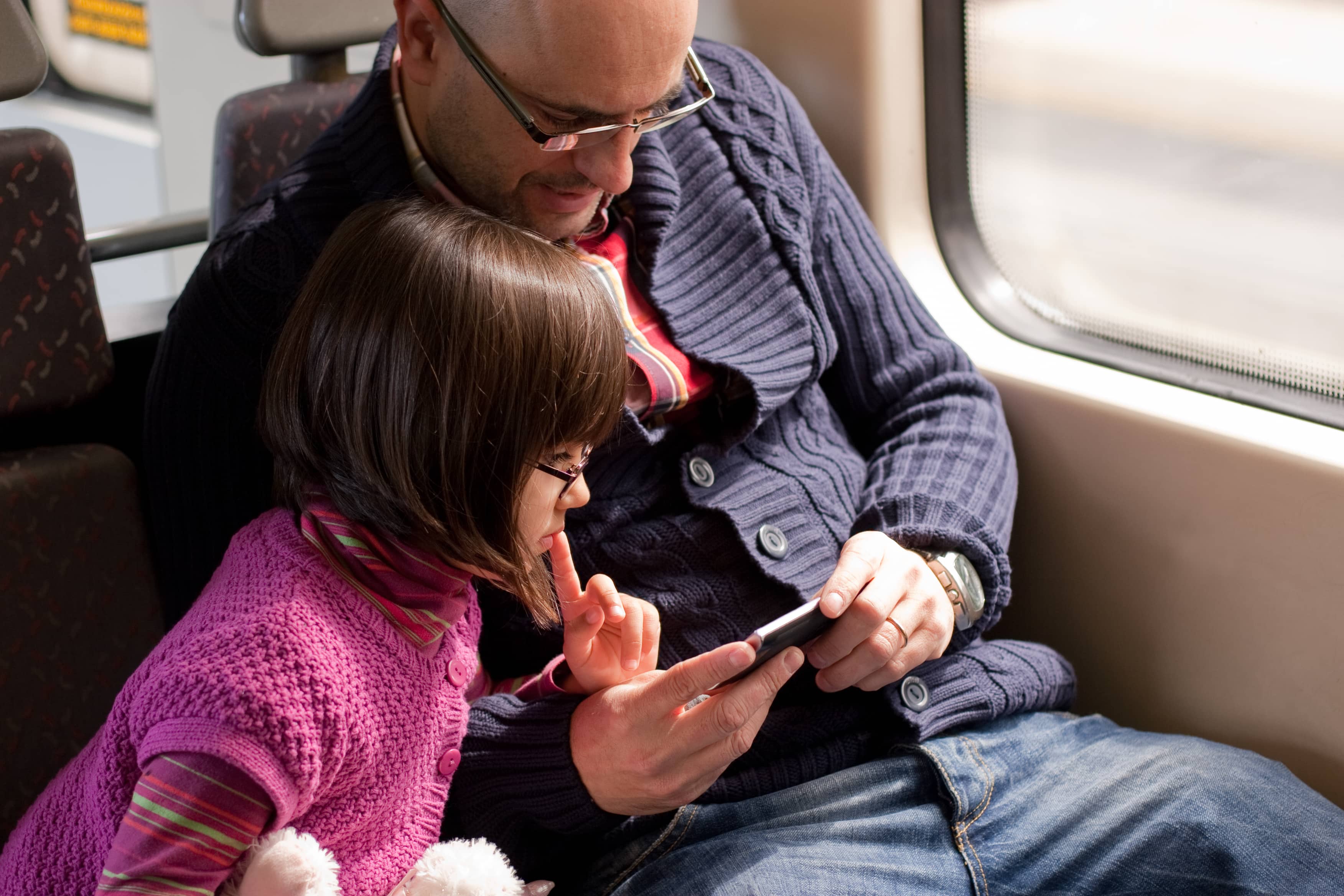 Avanti Trains: A father and daughter watch a video on his phone as they travel through the countryside on a train.