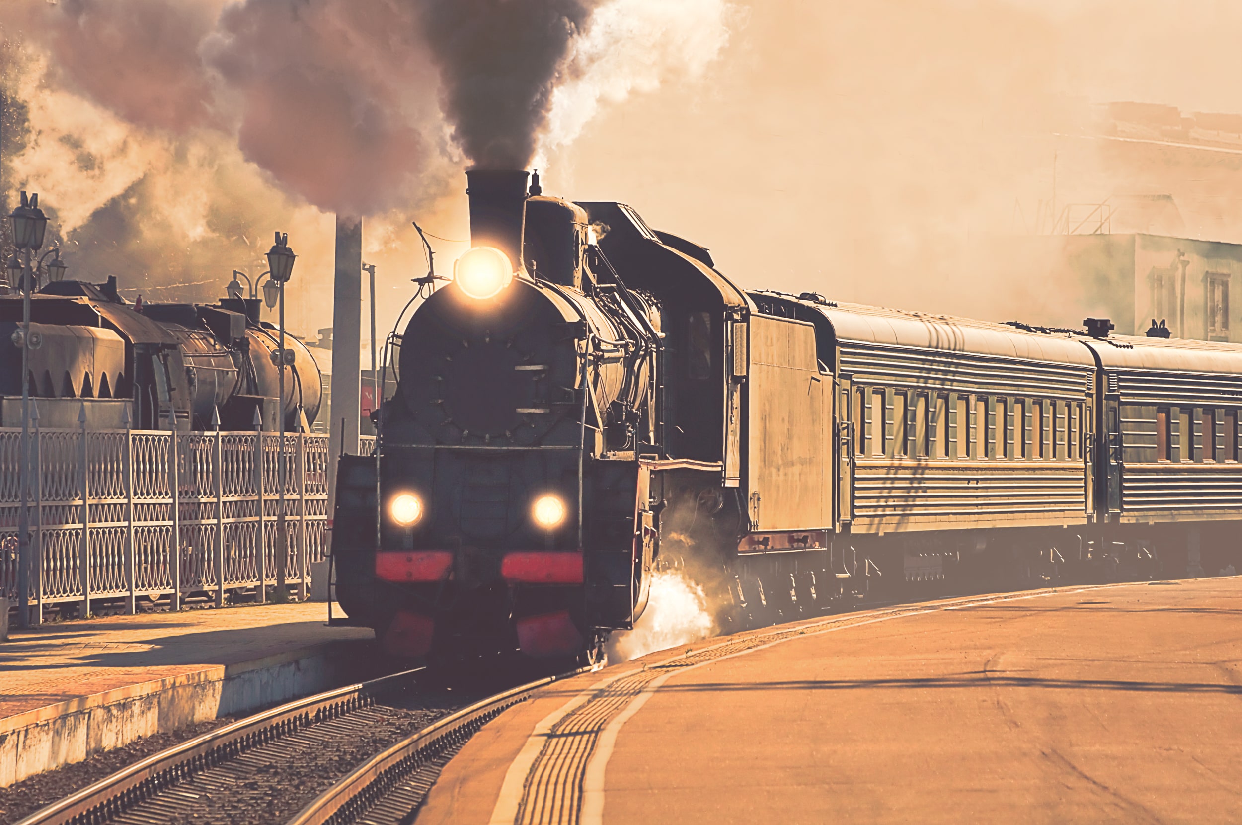 West Coast Train Line: A sepia photograph of an old steam train that’s moving through an empty station.