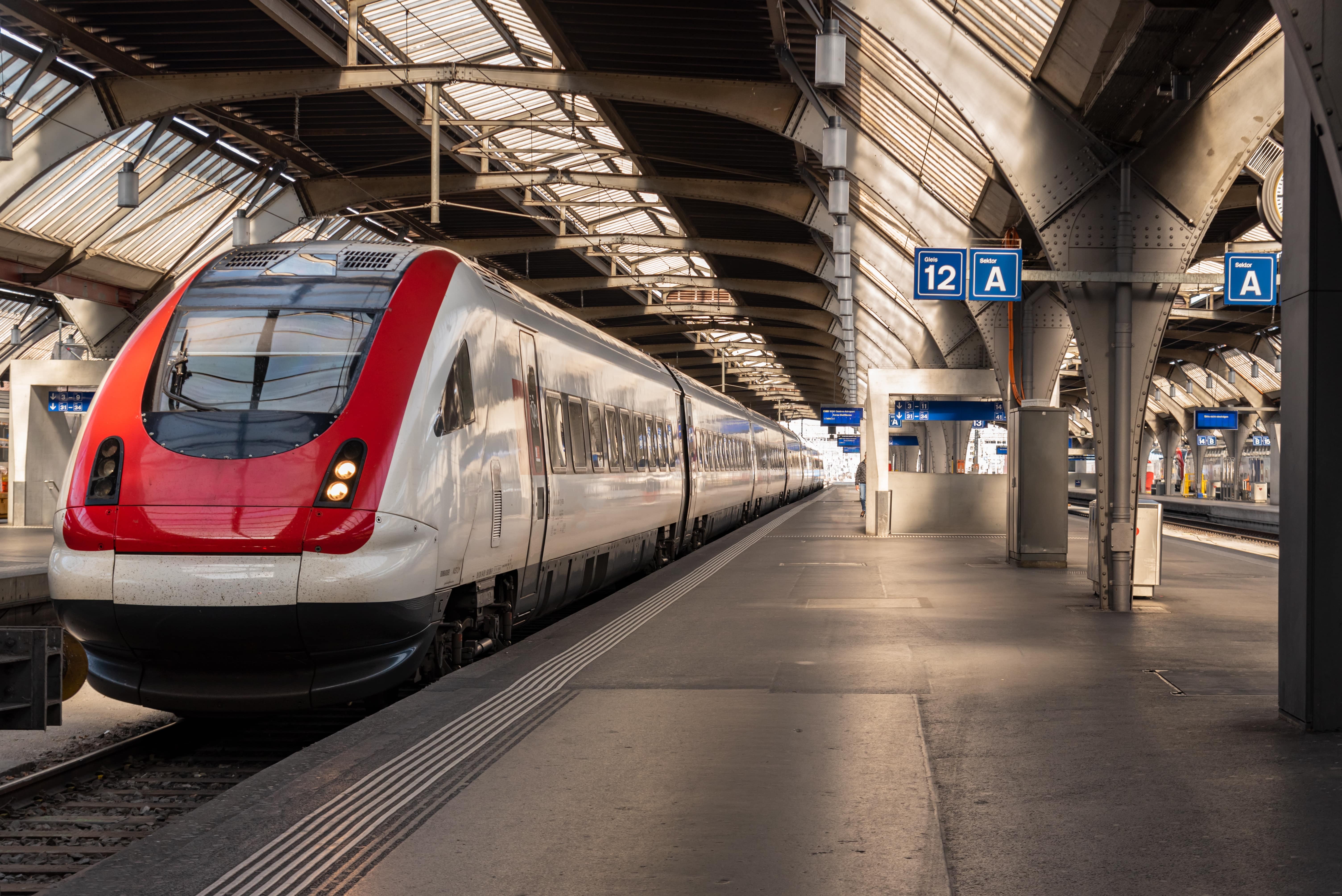 West Coast Train Line: A red and grey train sits stationary at an empty station during the day.
