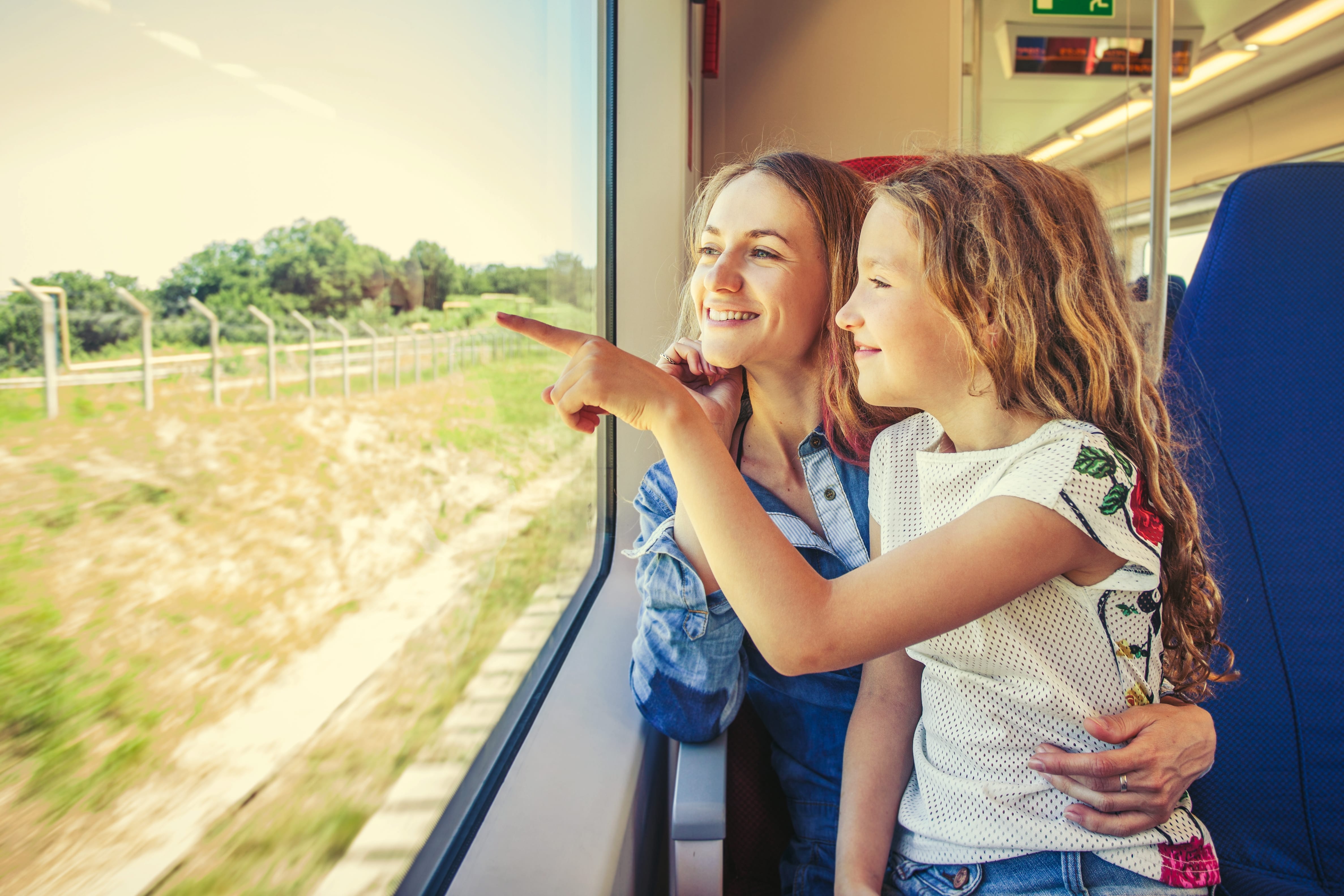 West Coast Train Line: A woman and a young girl sit on a train, as the girl points out the window at a passing field.
