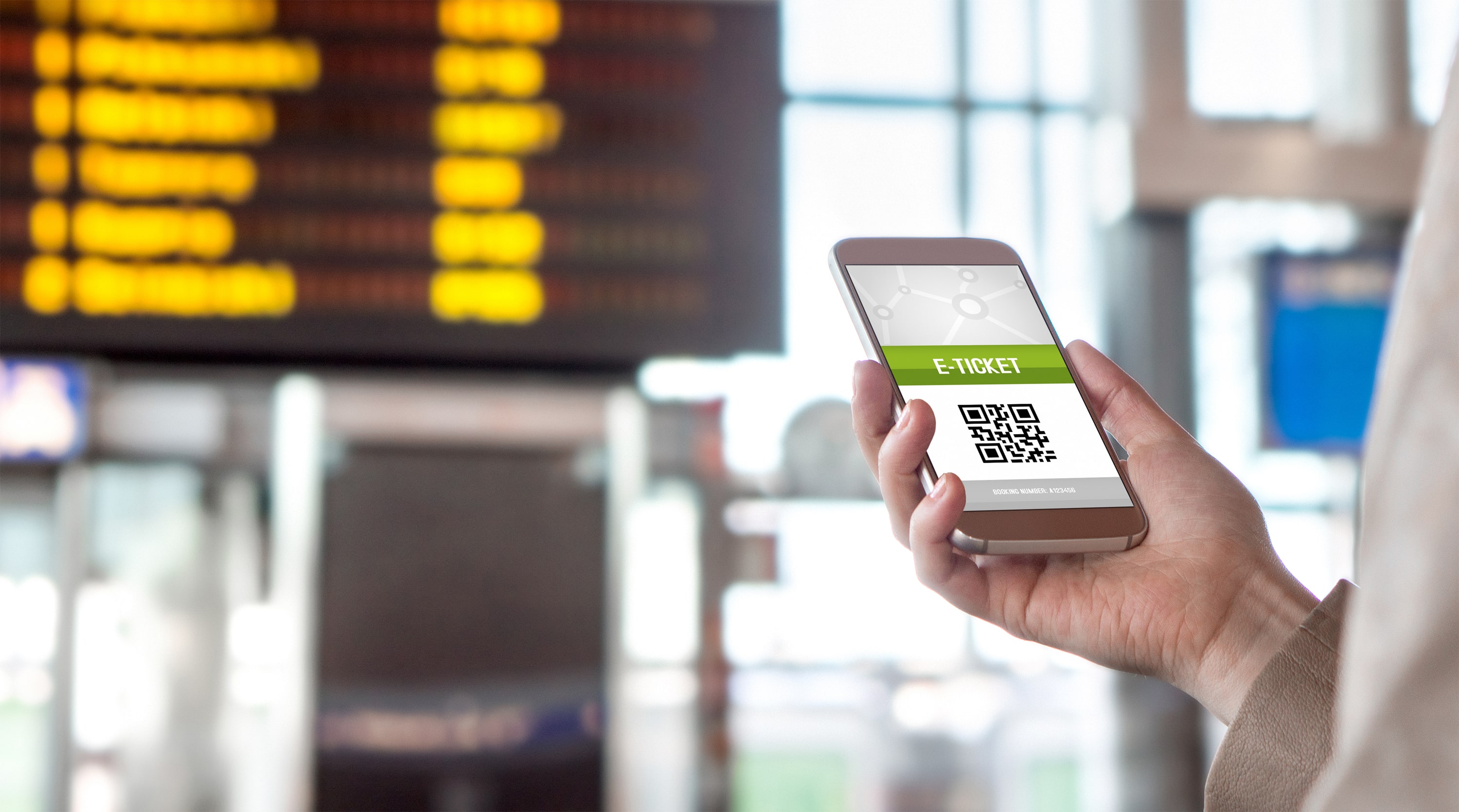 Train Ticket Design: Someone holding a smartphone displaying an e-ticket with a QR code at a train station, with a blurred departure board in the background