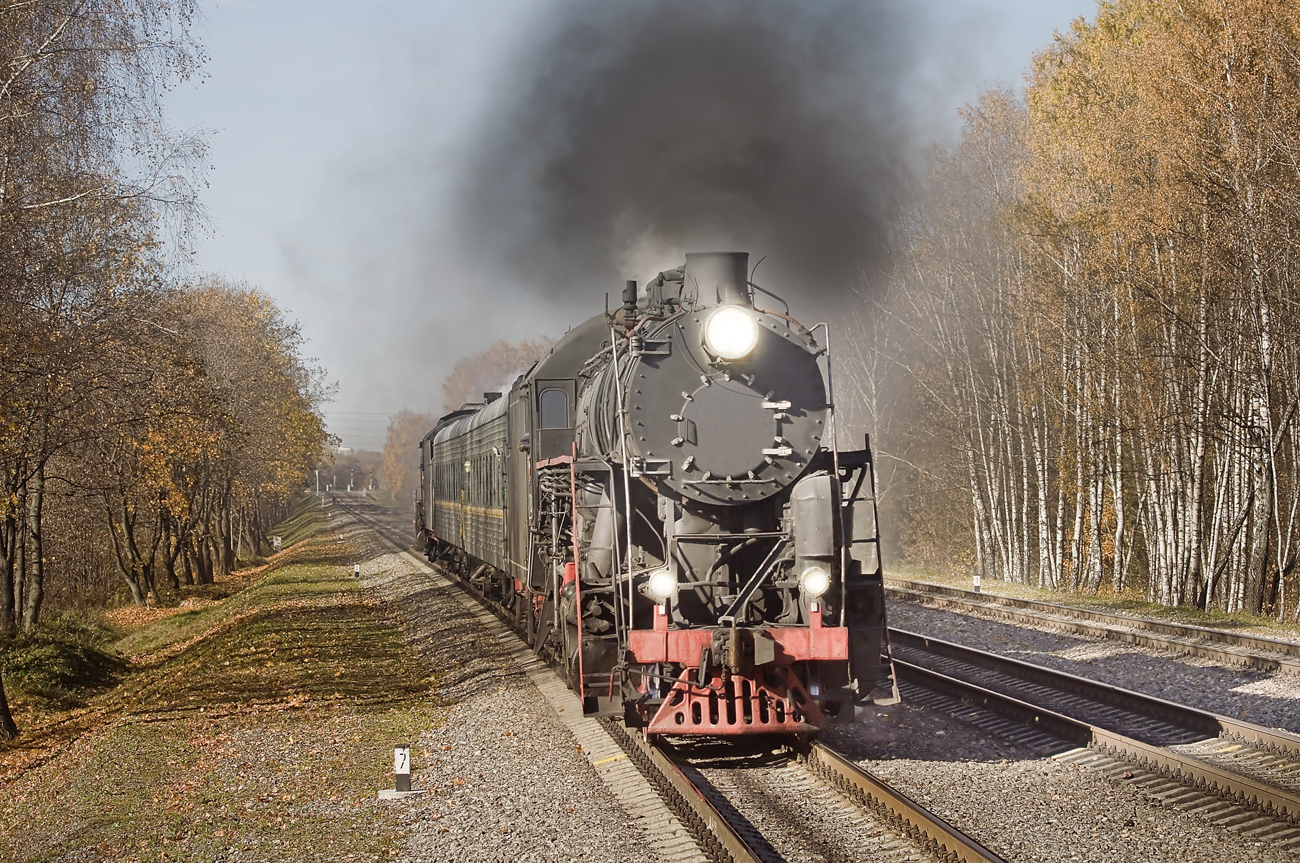 Rail Queens: Vintage steam locomotive with a bright headlamp and billowing black smoke travelling along railway tracks through an autumn landscape