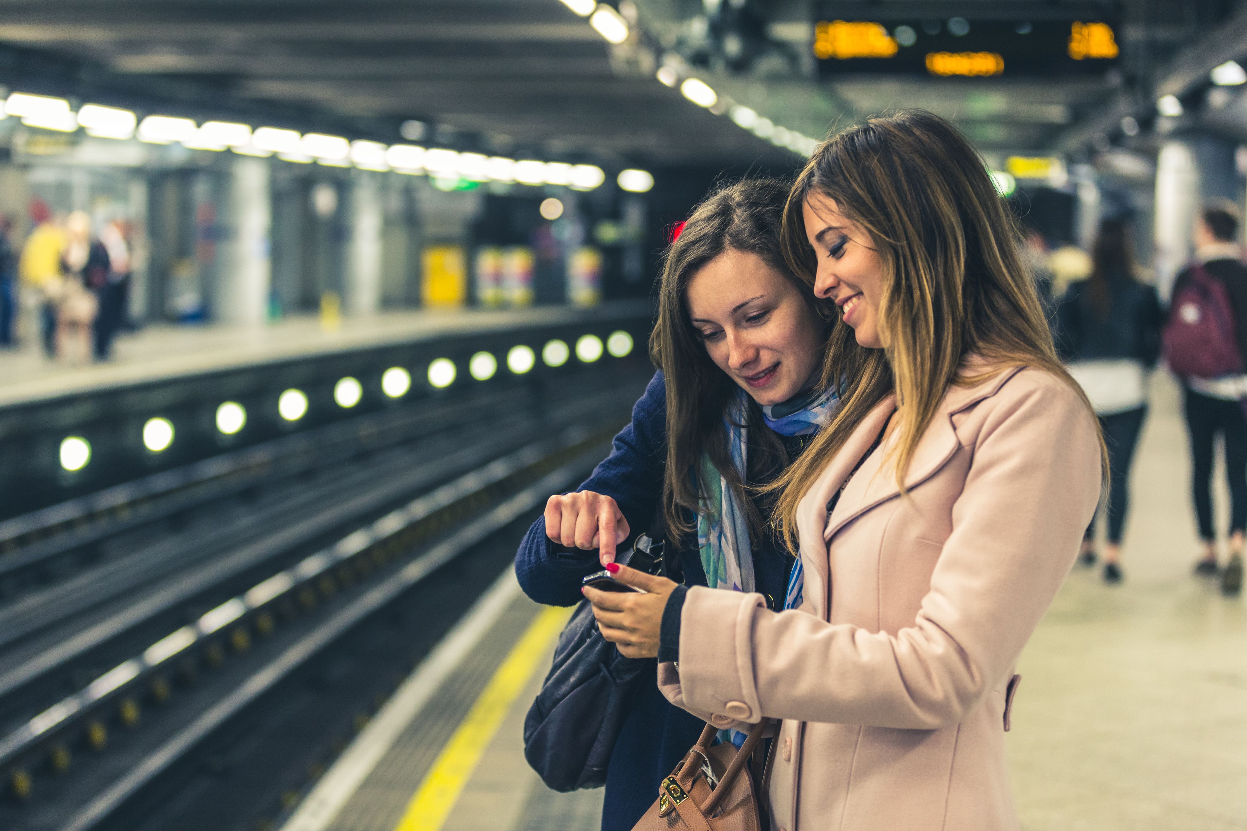 Train Classes: Two women looking at a phone whilst waiting for a train.