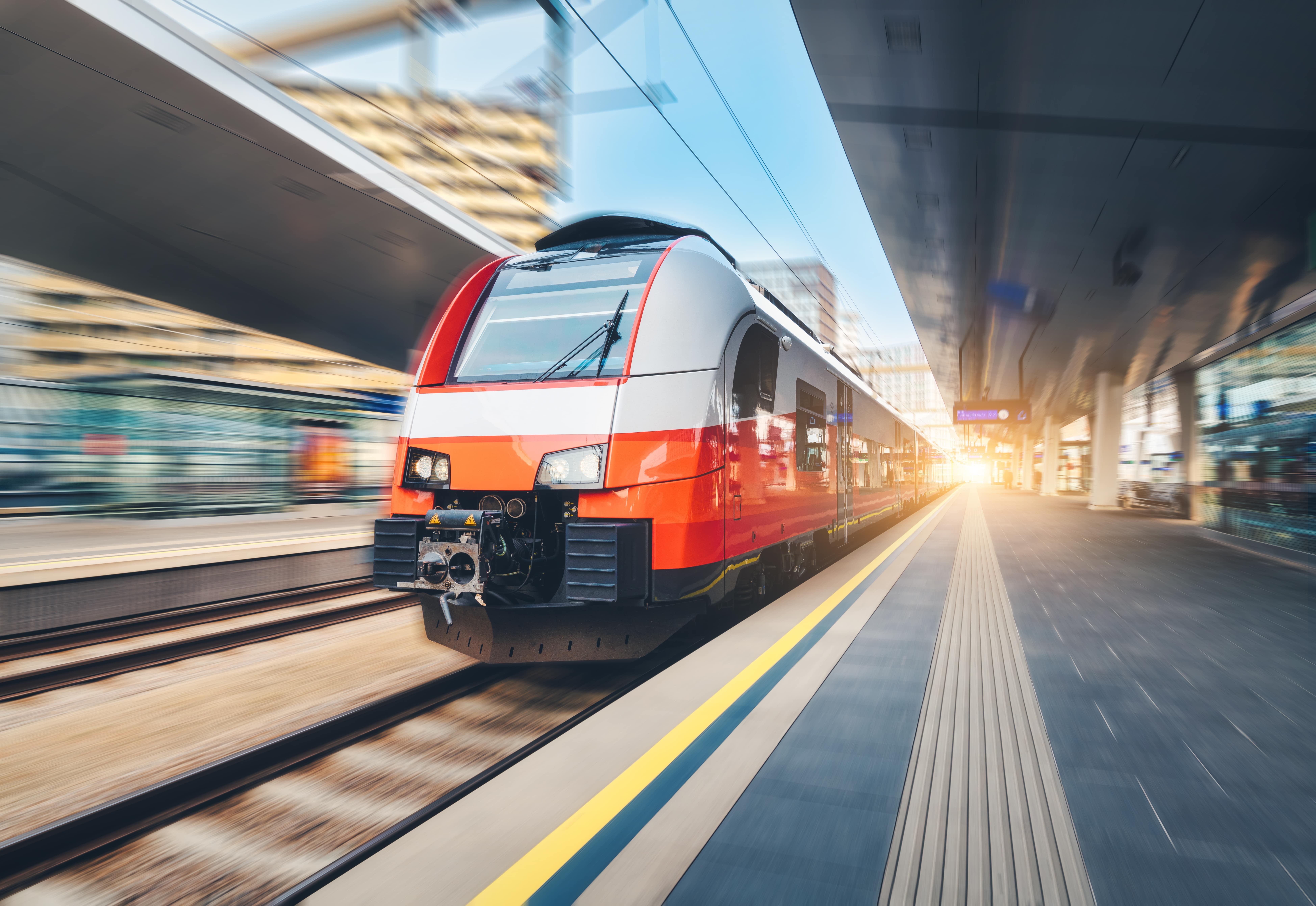 Trains in the UK: A grey and orange train prepares to leave a quiet station during the daytime.