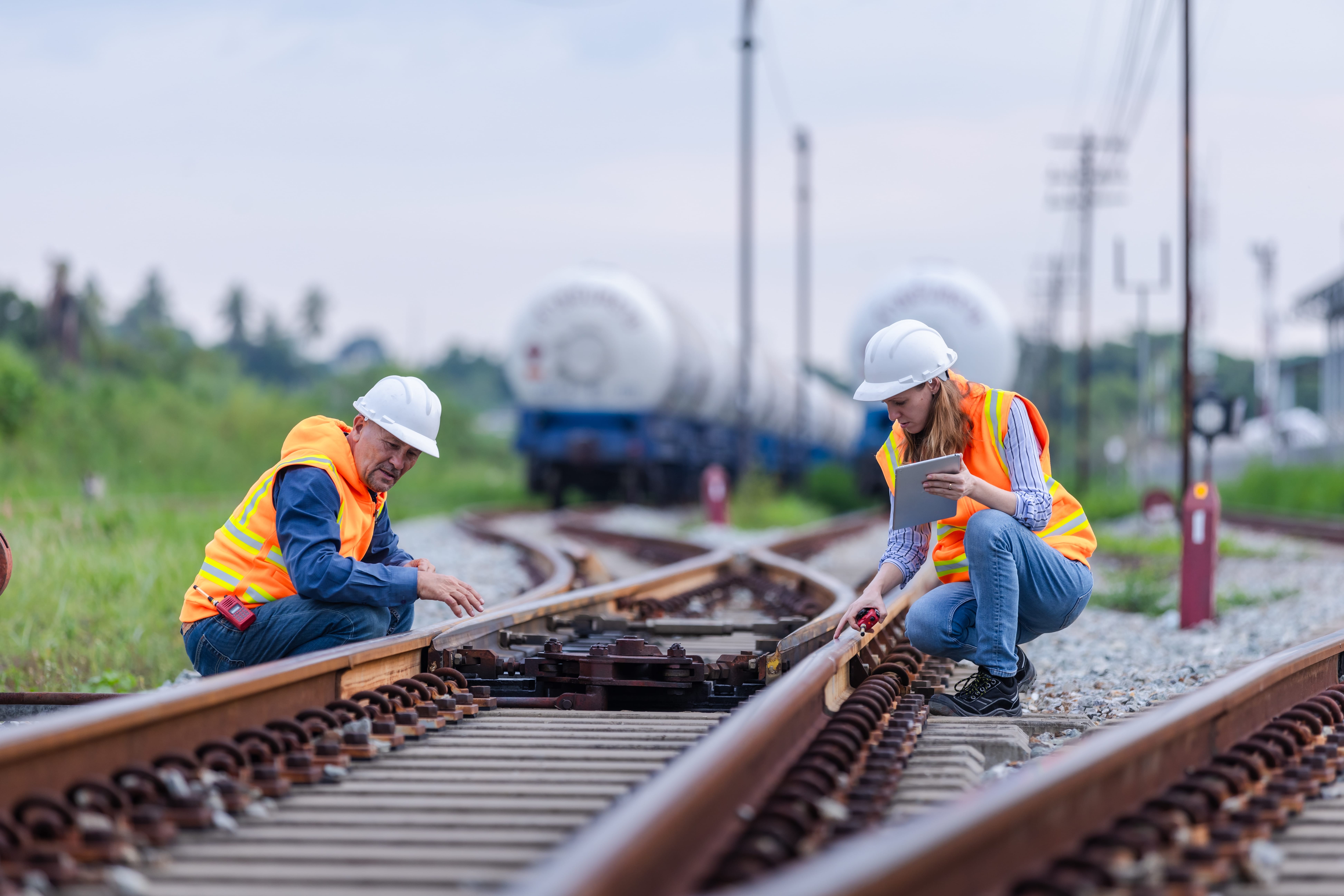 Jobs in Rail: Two railway workers wearing hard hats and high-visibility vests inspecting and maintaining a railway switch