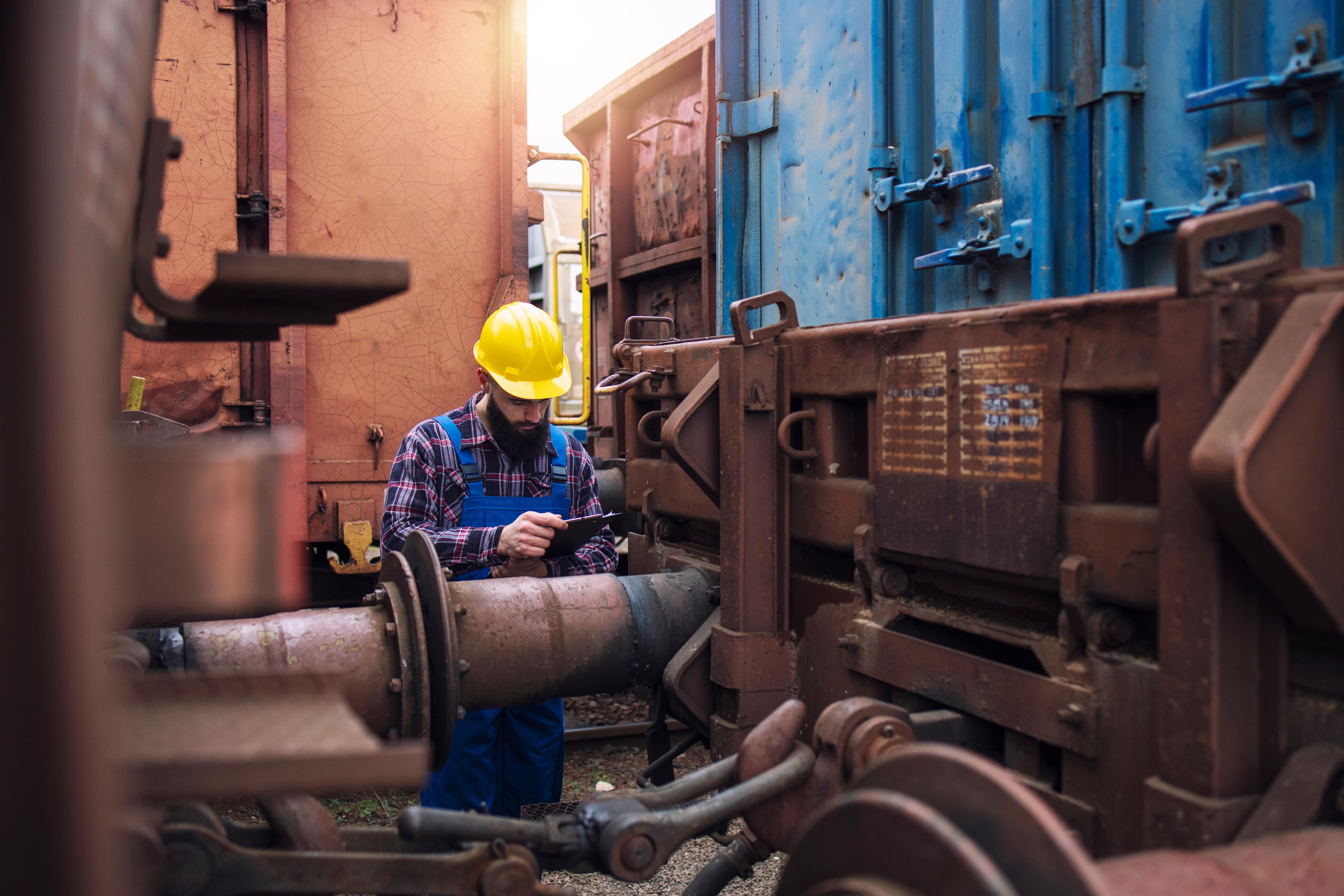Jobs in Rail: A young man in a yellow hard hat checking on the cargo containers of a freight train.