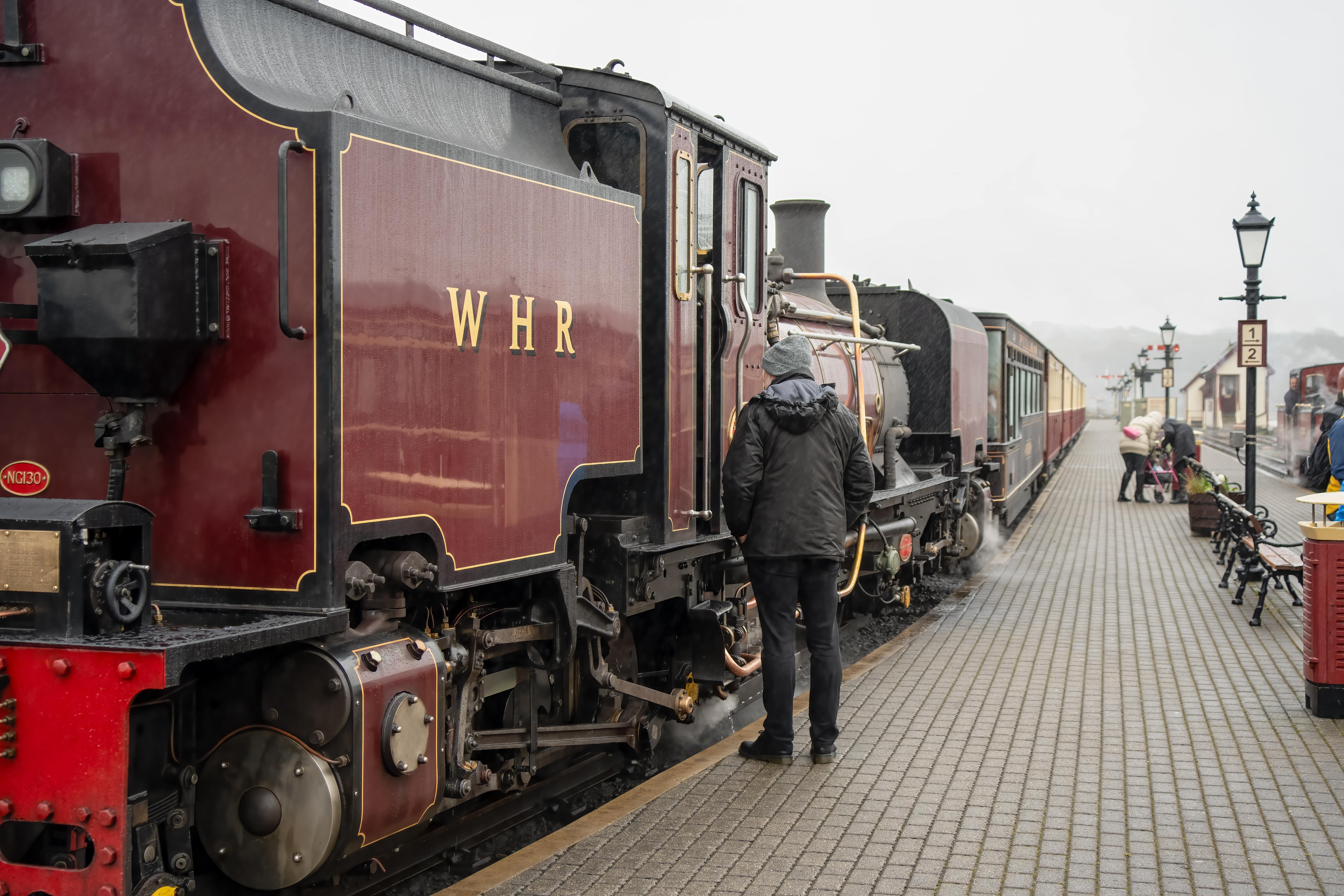 Bicentennial: Vintage steam train at a station platform, with a passenger in a hooded jacket inspecting the locomotive