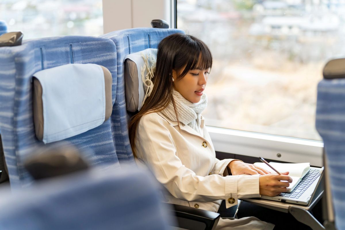 Writing Rail Books 2 Train Books: A young woman writes on a notepad at her seat on a train.