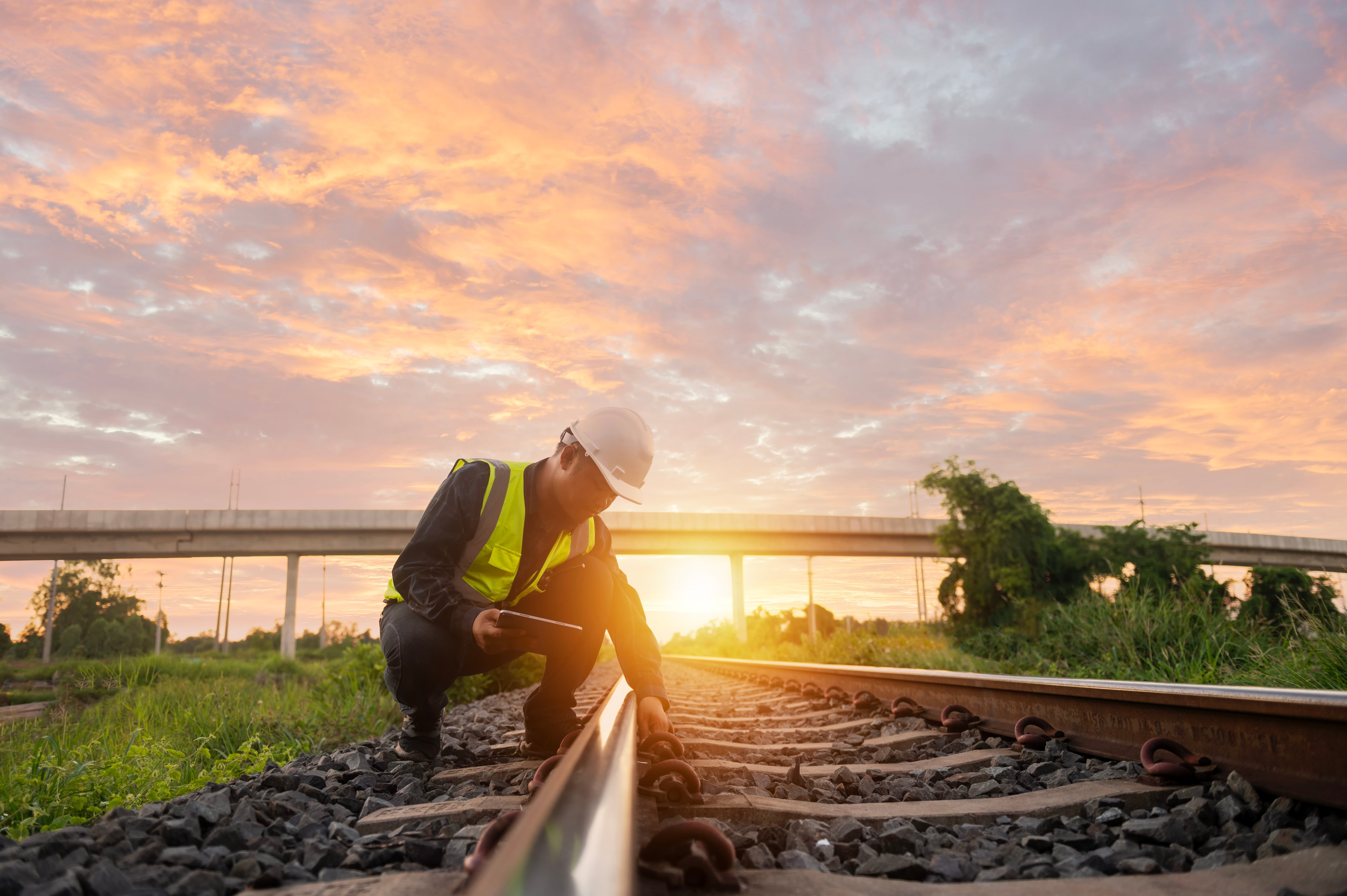 Eco-Friendly Transportation: A railway engineer inspects rail tracks to a backdrop of a setting sun.