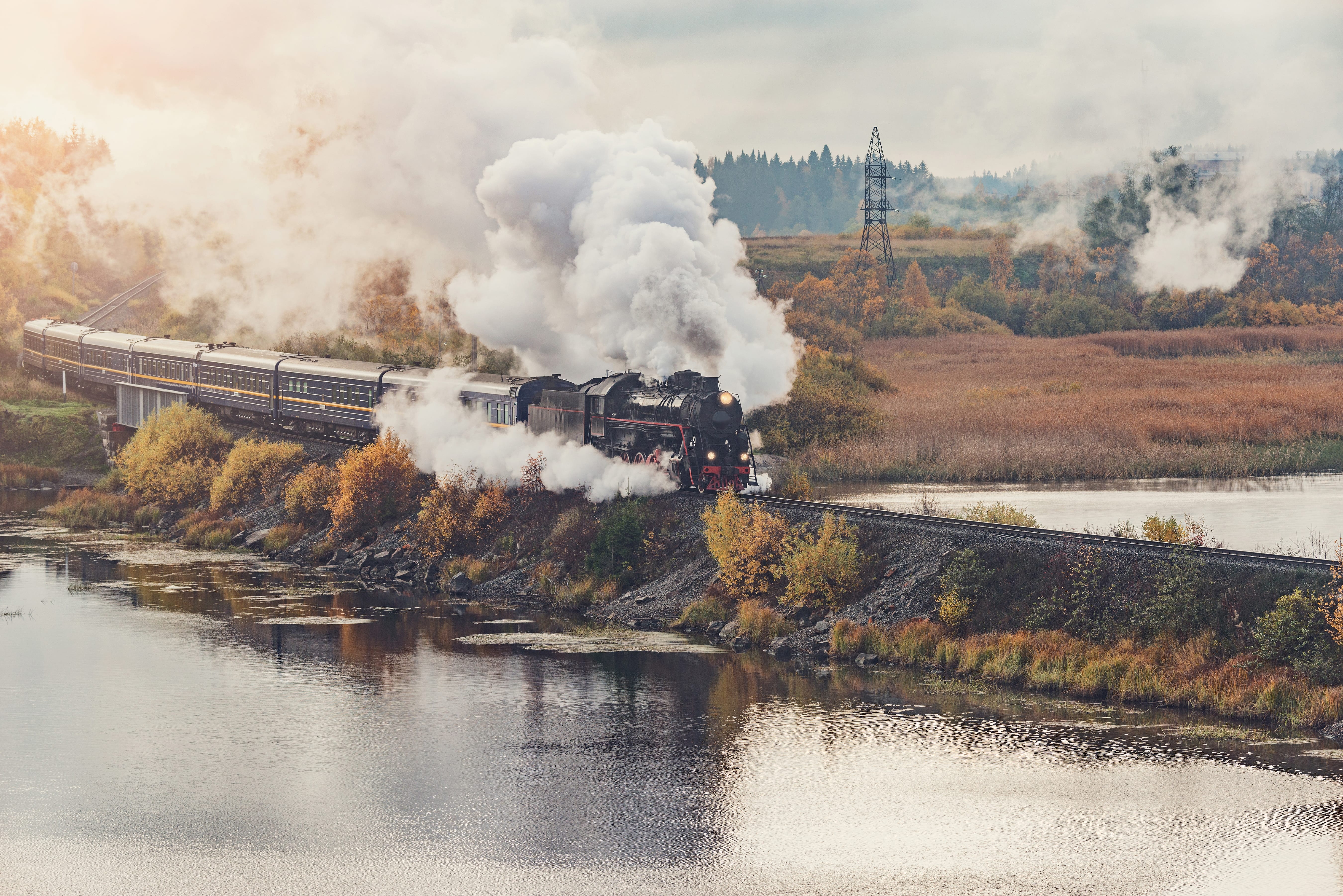 Steam Train Experiences: A steam train travels along a lake during sunrise.