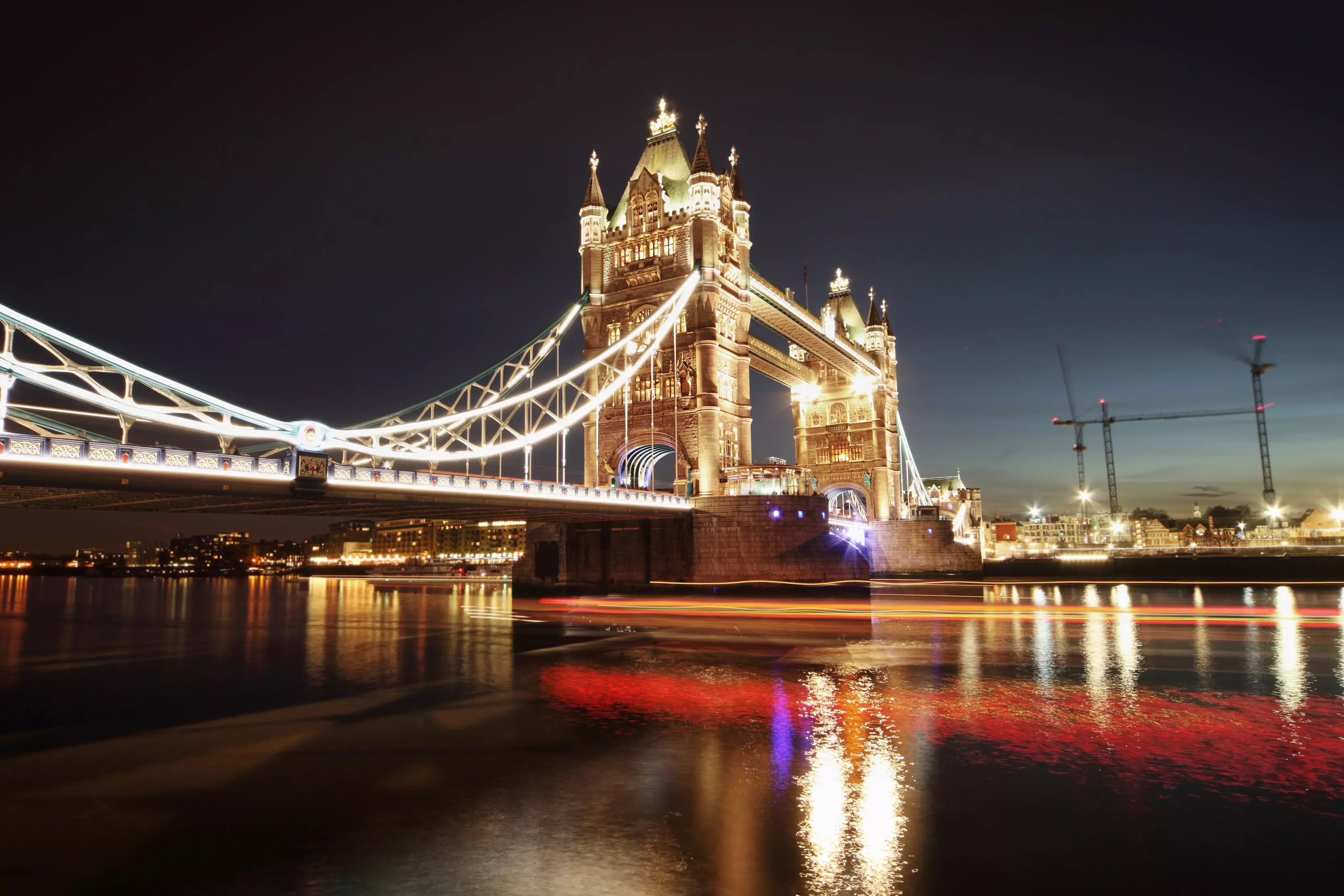 A wide-angle shot of London Bridge illuminated by lights at night.
