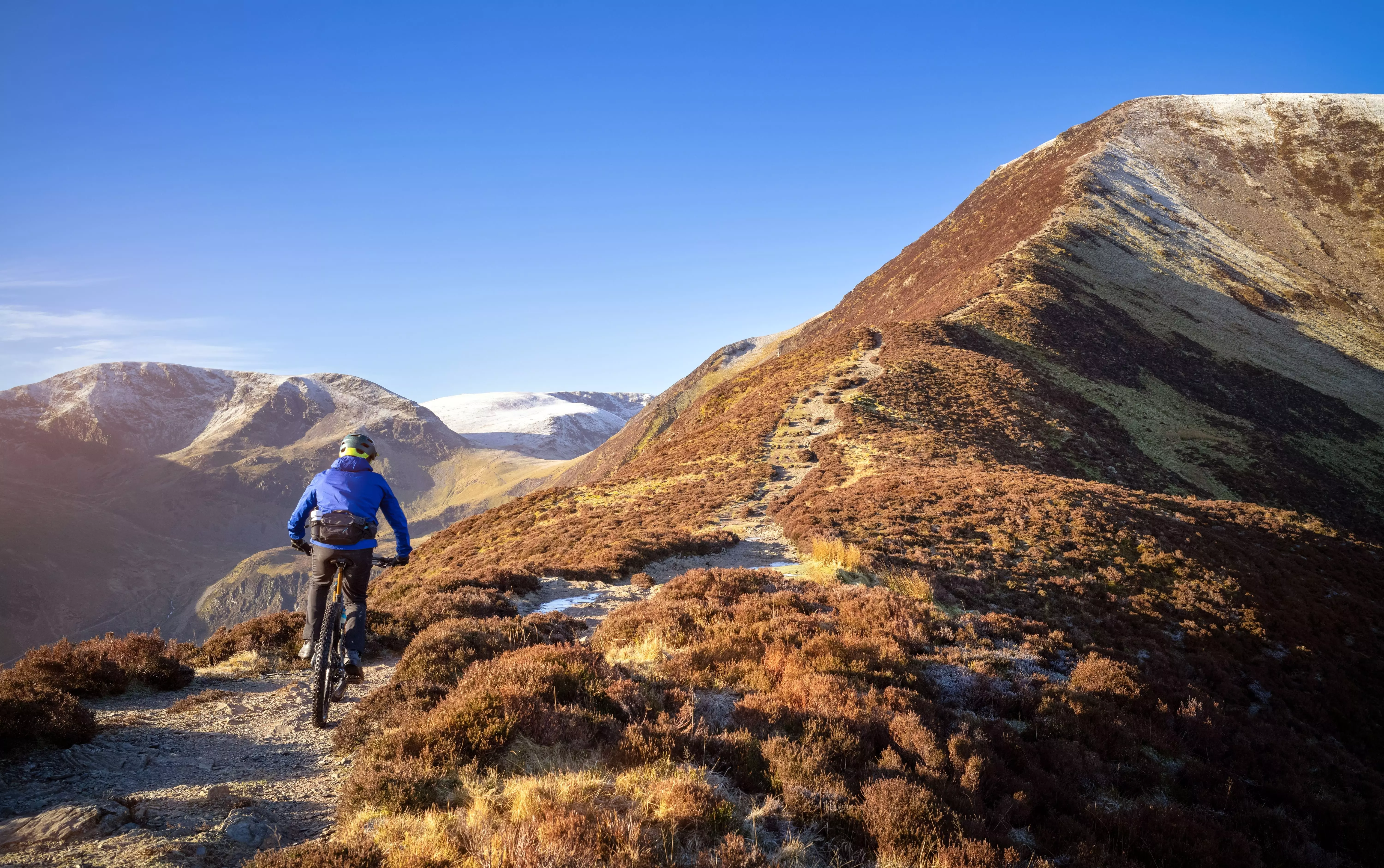 A mountain biker riding up the trail to the summit of Grisedale Pike with Crag Hill in the distance in Lake District.