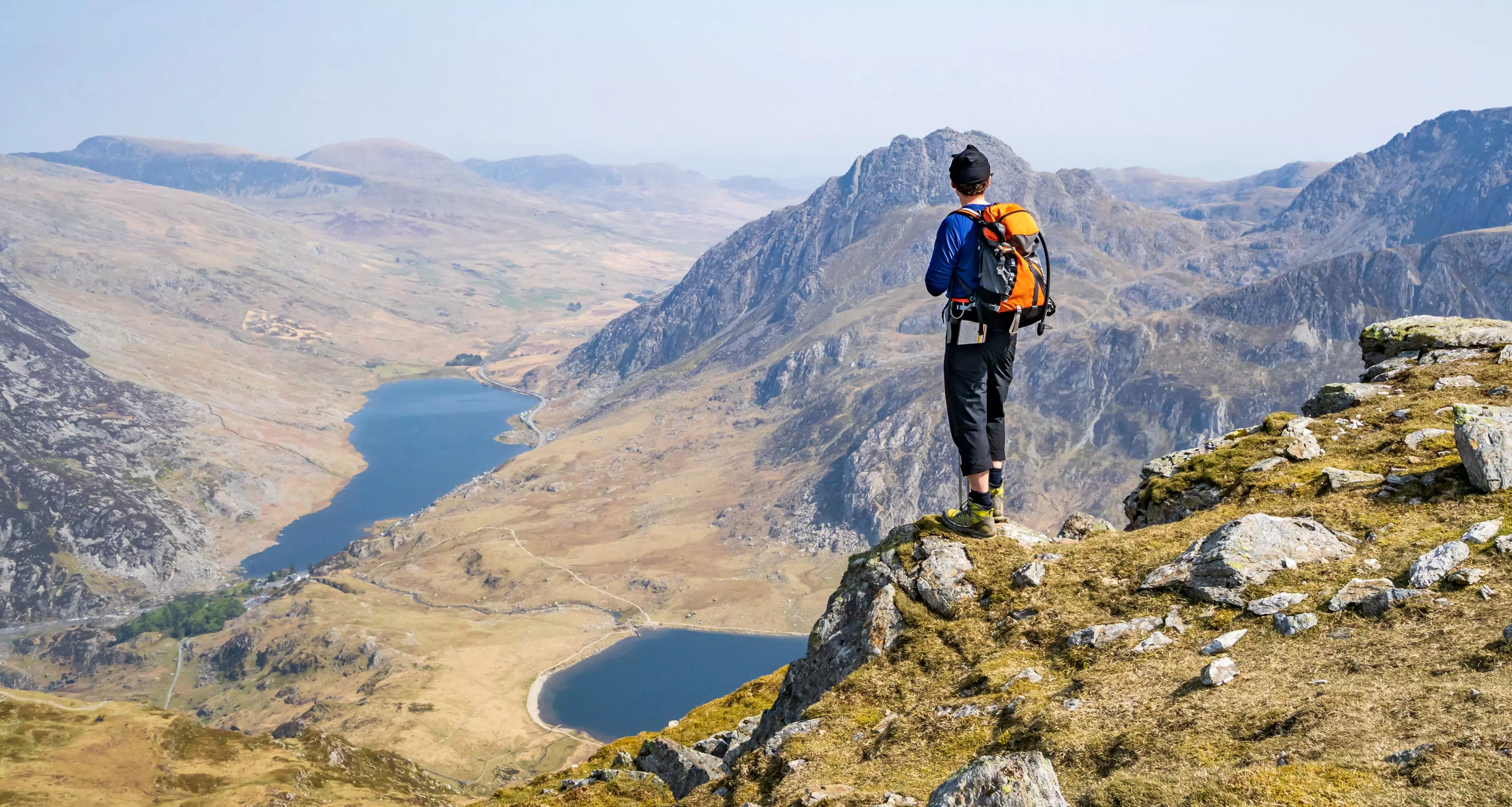 A hiker, stands on top a Y Garn ridge overlooking Tryfan, the Carneddau and the Ogwen Valley with the Llyn Idwal and Llyn Ogwen below in Snowdonia National Park, Wales